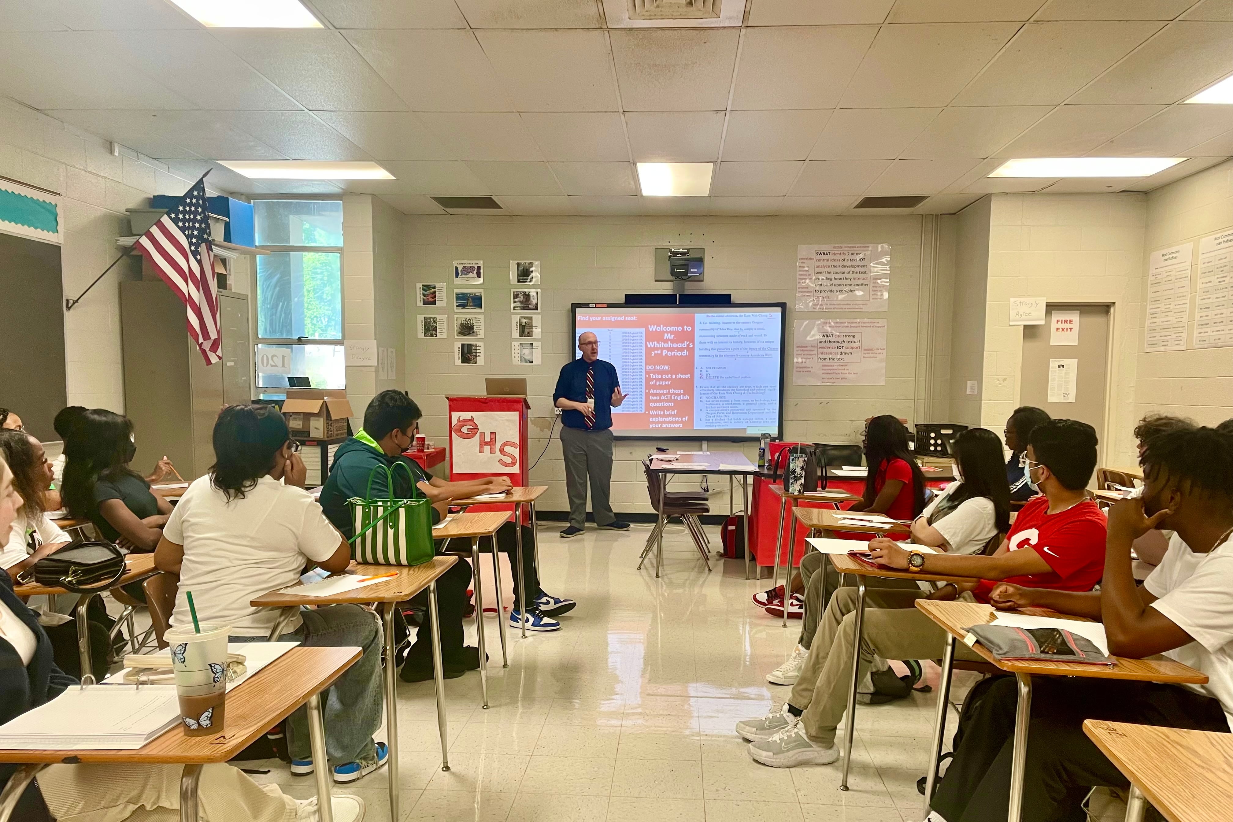 A man standing in front of a smart board teaches a classroom of students