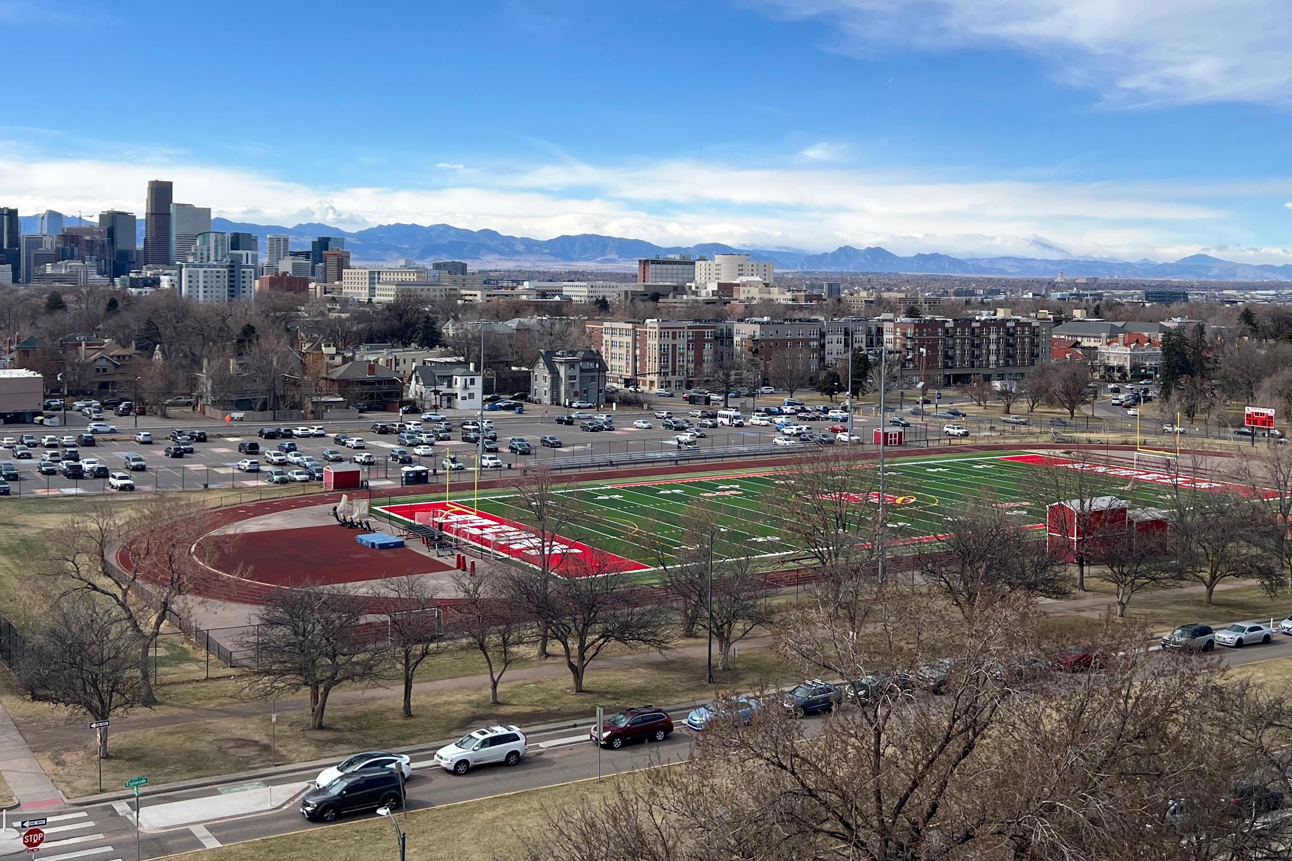 An aerial view of a high school football field with the Denver skyline in the background.