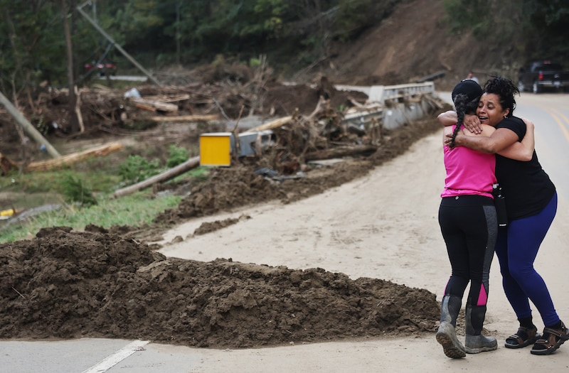 Two women hug in front of debris from a hurricane.