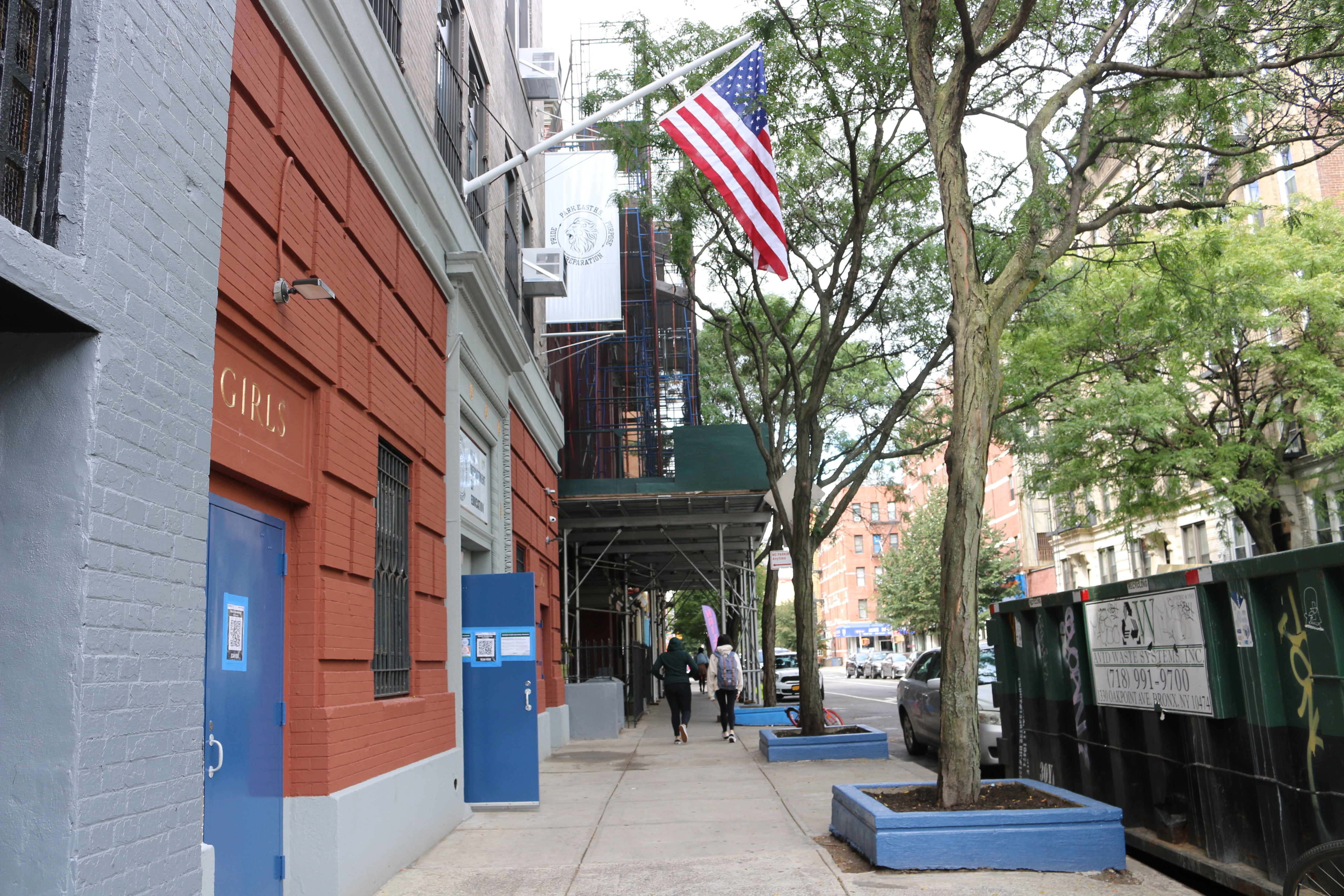 An American flag hangs above the entrance of a red brick building with blue doors.