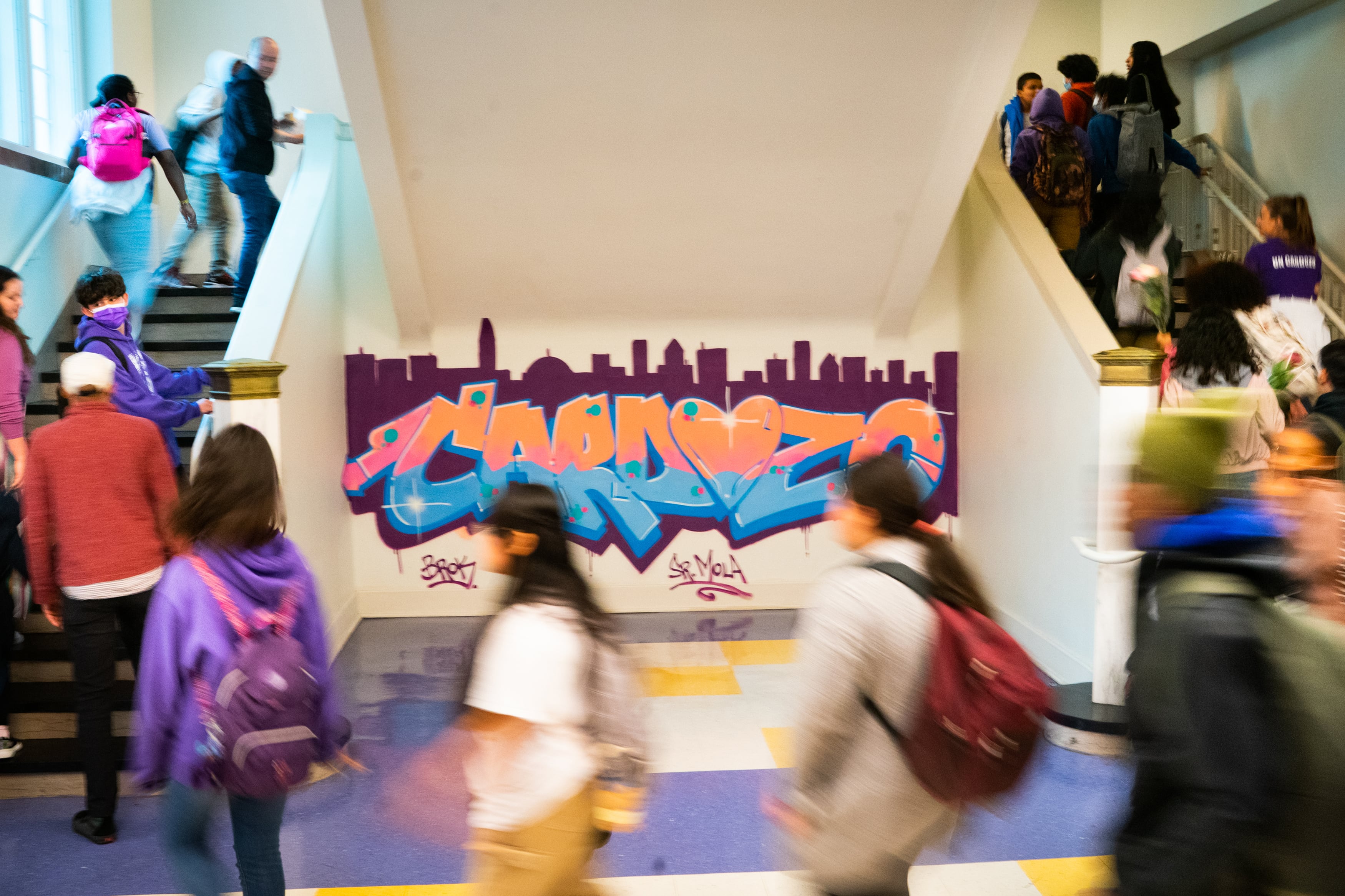 Students walk in a line from one set of stairs to another with a grafiti artwork on the wall in the middle.