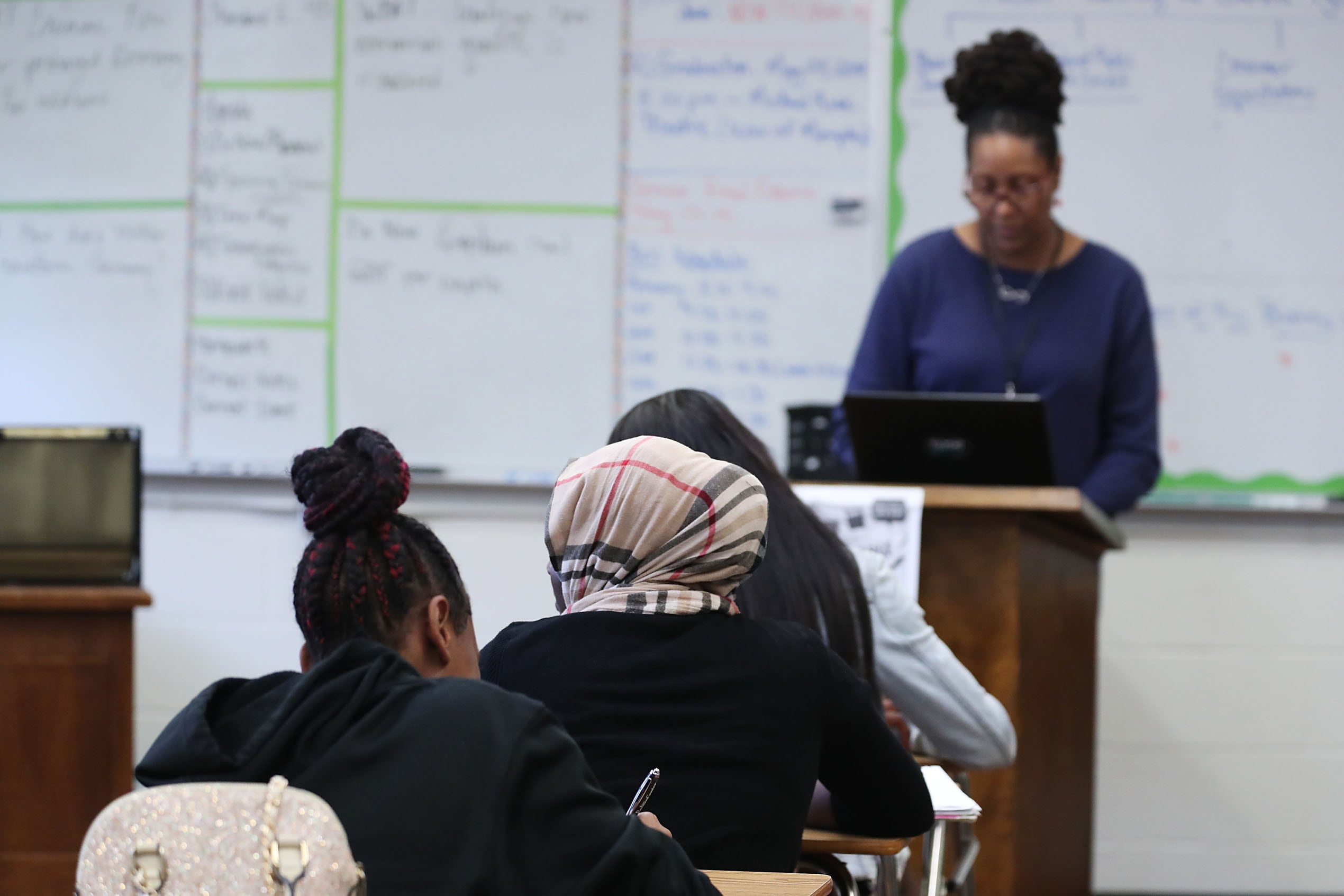 Teacher stands at a podium in front of students in a classroom