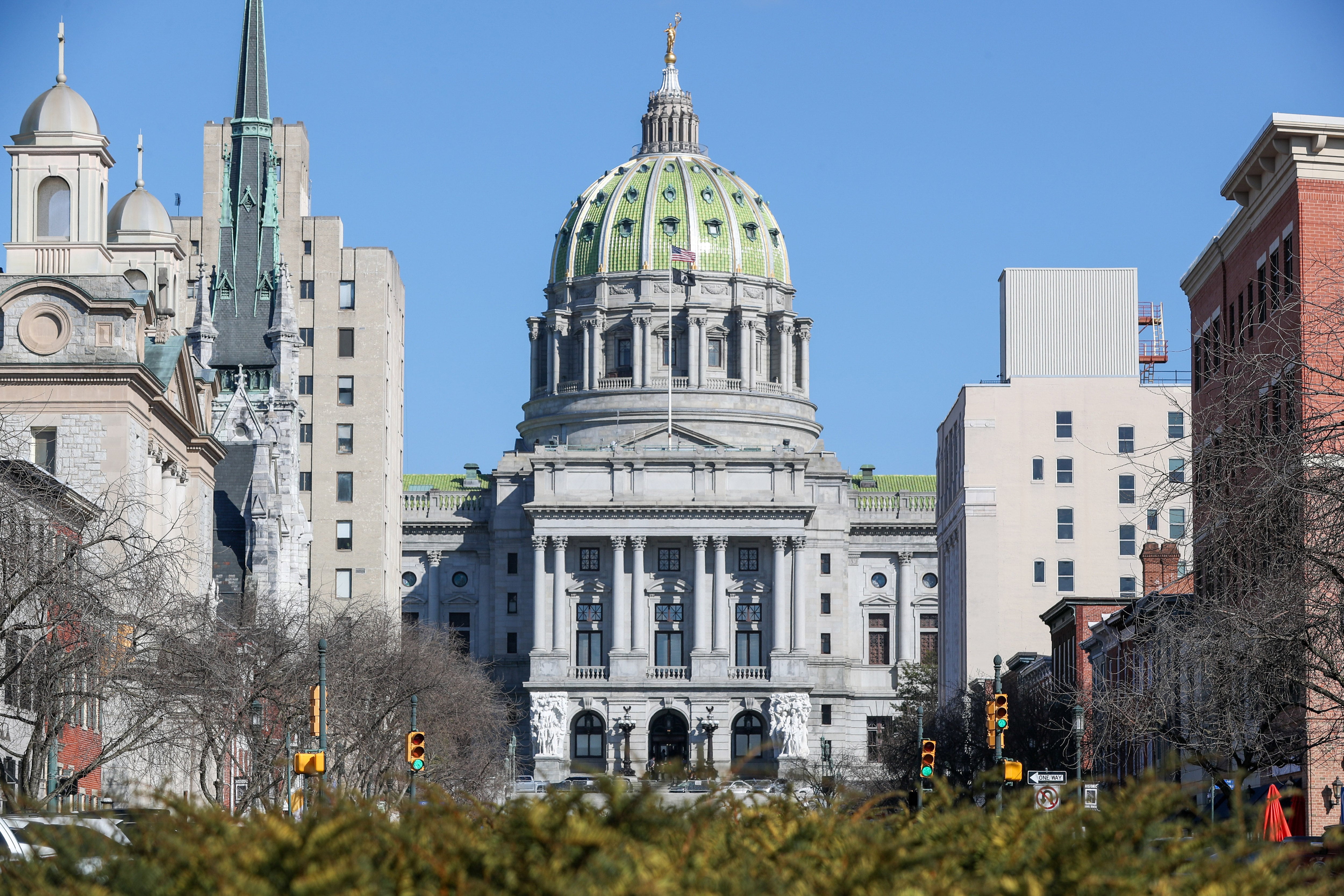 A large white stone capitol building with trees, cars and buildings around.