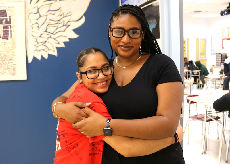 A woman in a black shirt hugs a girl with a red shirt.