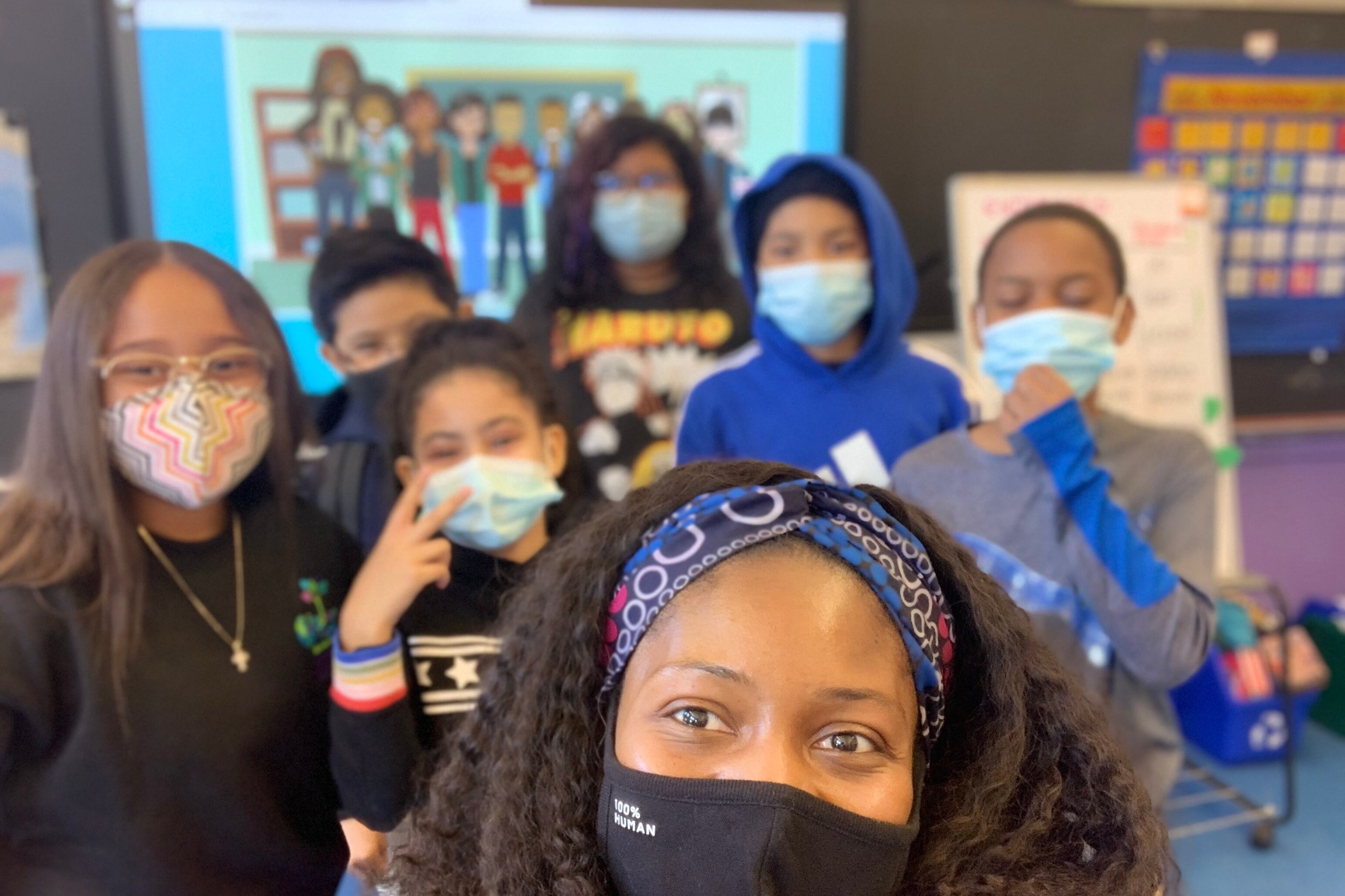 A woman in a mask is pictured with six masked students.