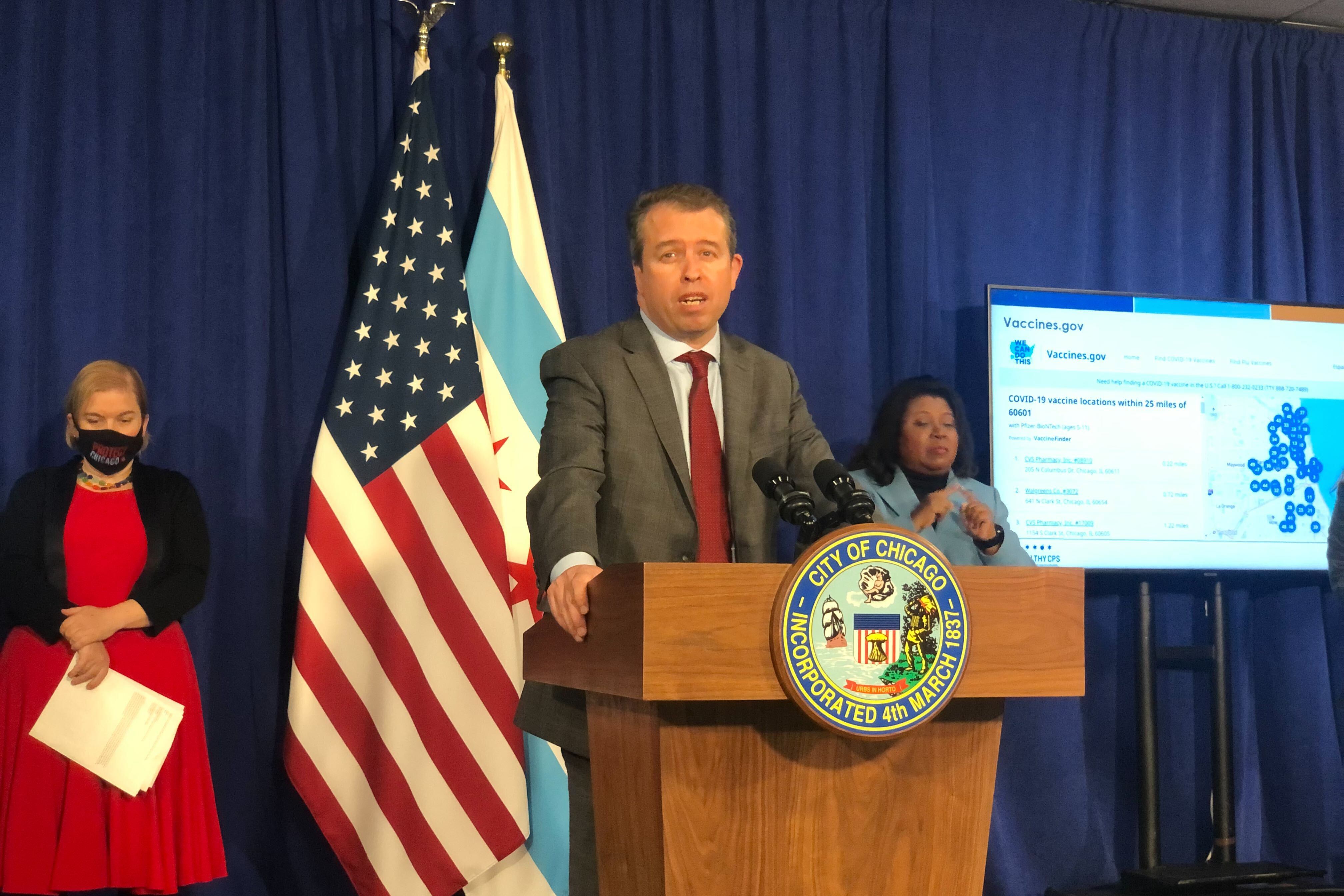 A man stands at a podium next to the United States and Chicago flag.