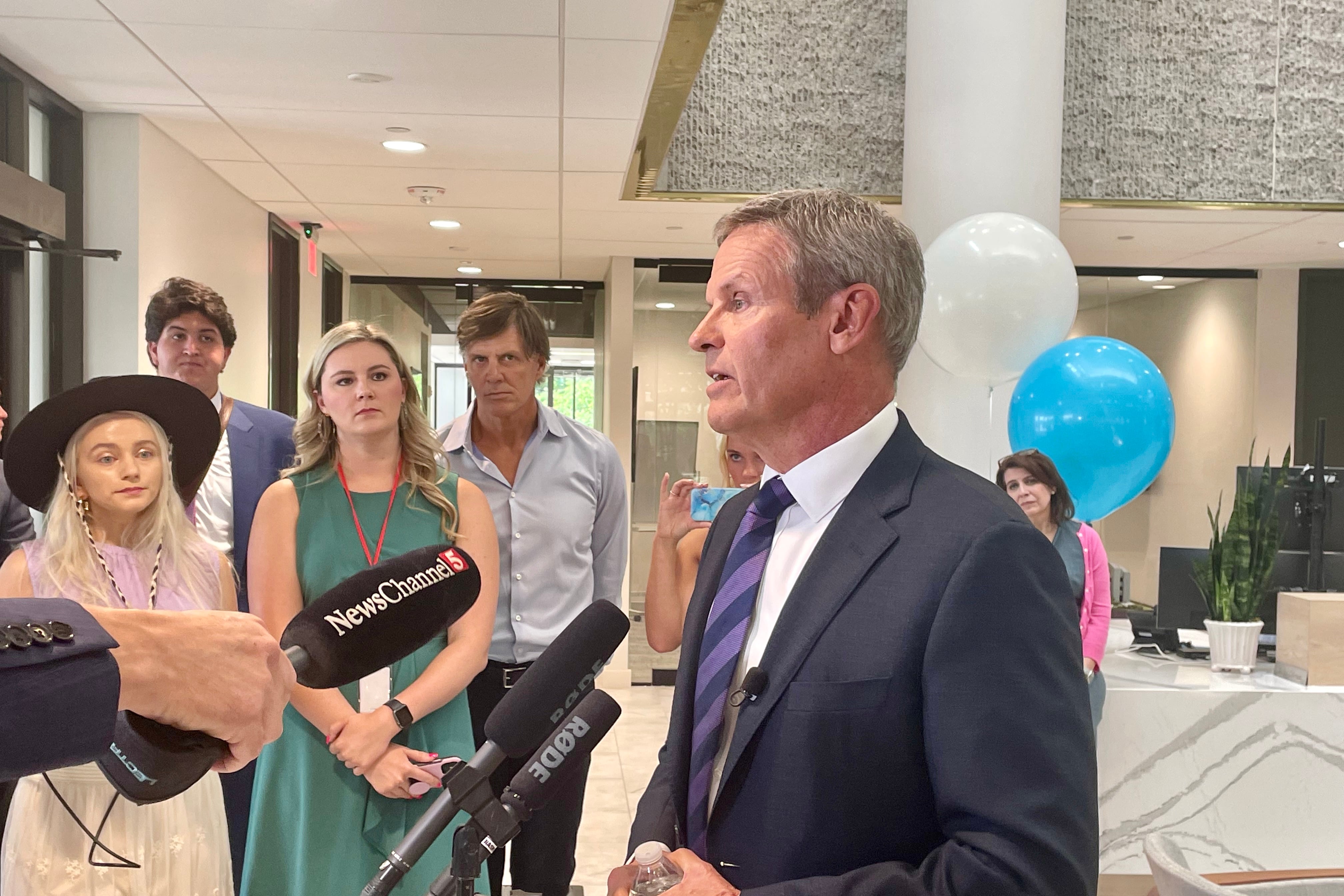 A man in a suit and tie speaks into several microphones.