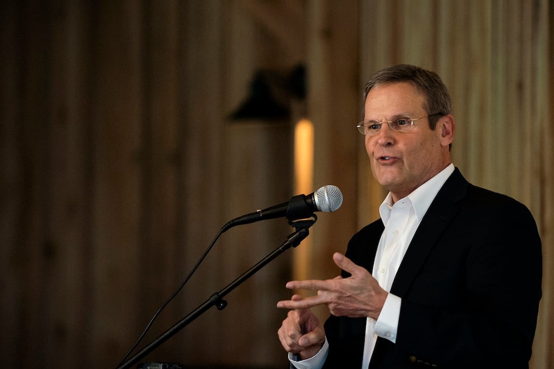 Man in a suit and wearing classes gestures while standing at a podium