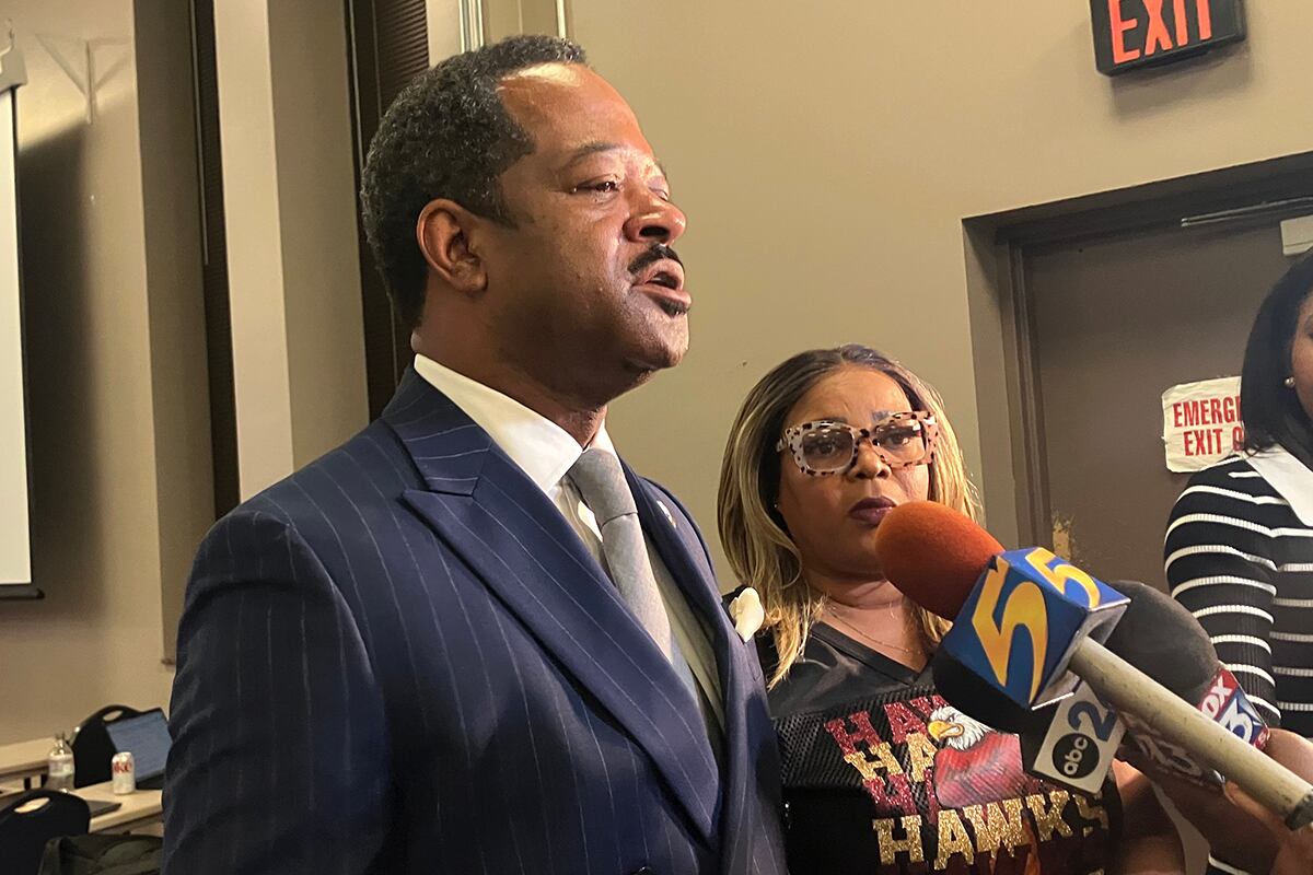 A man in a dark suit jacket speaks to reporters.