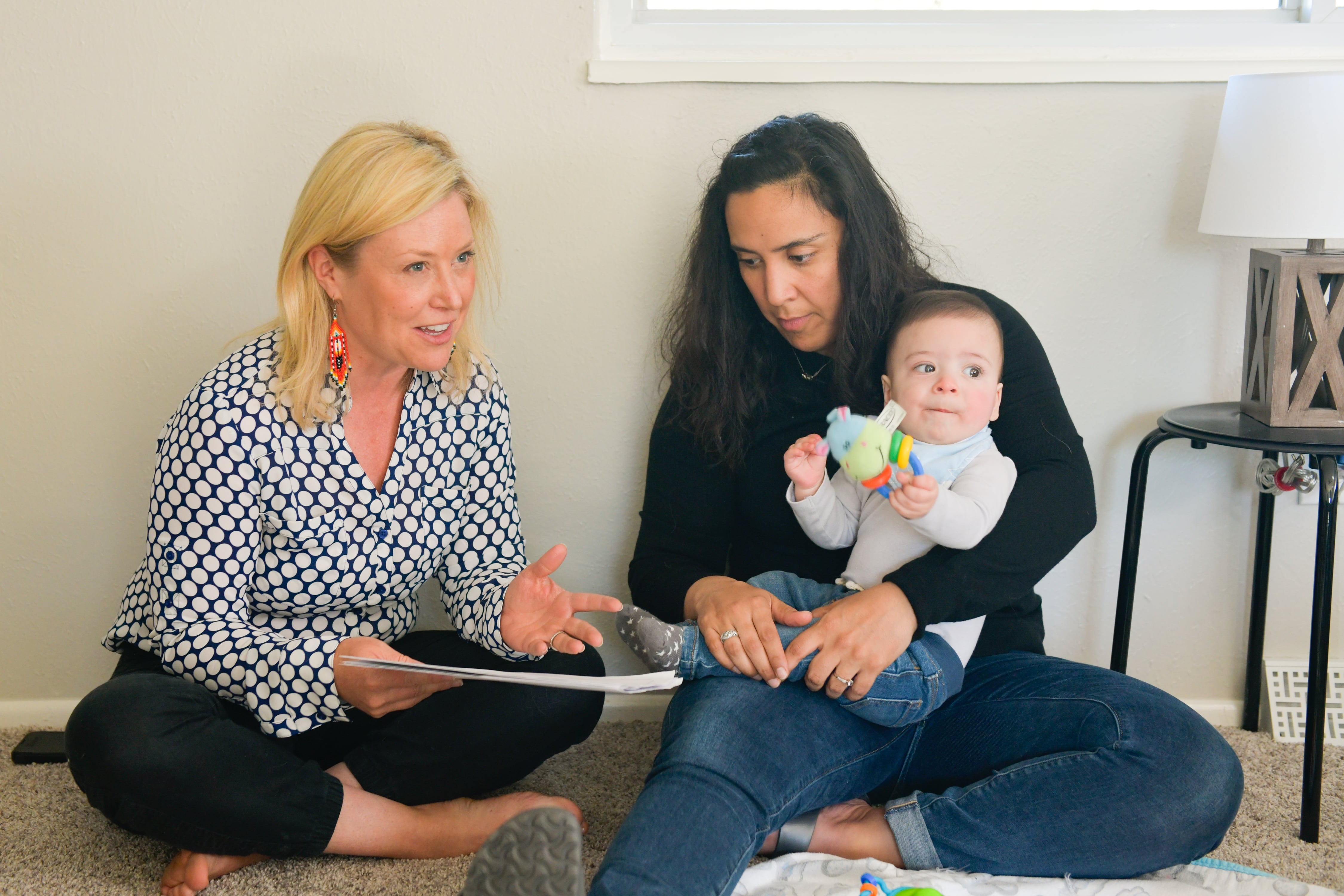 Two women sit on the floor reading a book to a child.