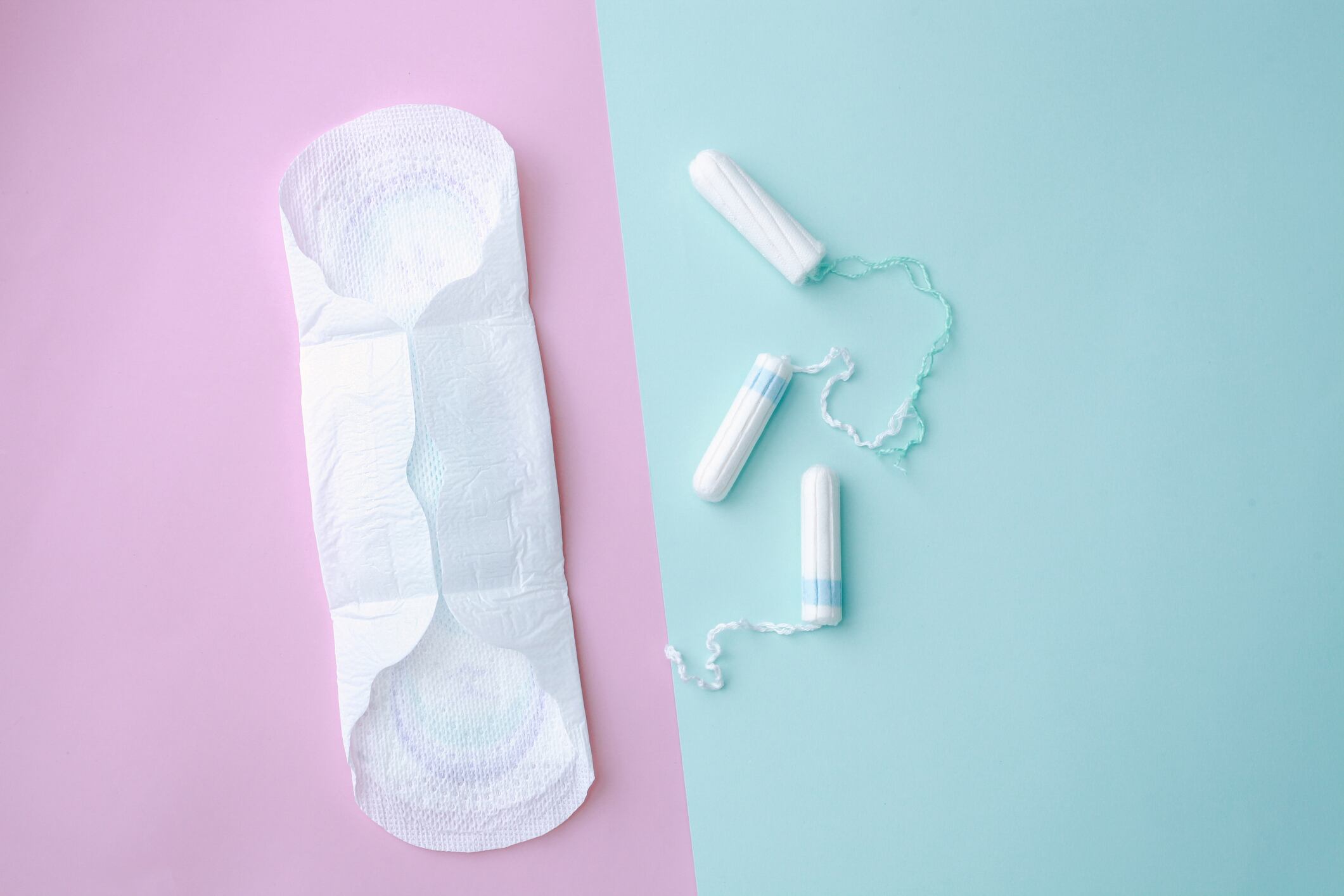 A menstrual pad sits against a pink background, next to three tampons that sit against a blue background.