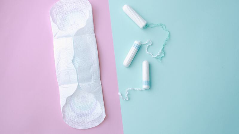 A menstrual pad sits against a pink background, next to three tampons that sit against a blue background.