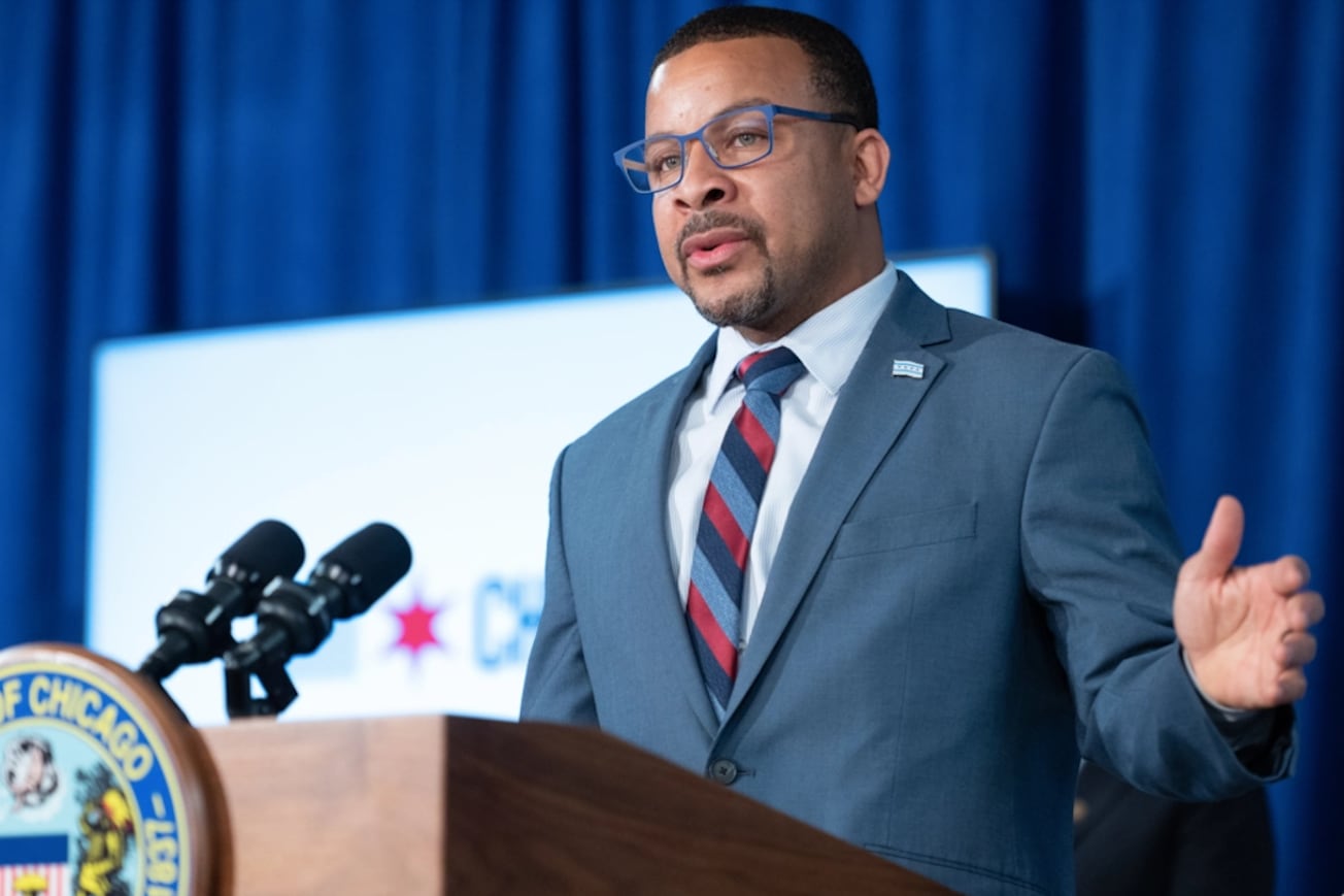 A man in a blue suit stands at a city hall lectern.