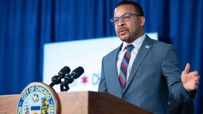 A man in a blue suit stands at a city hall lectern.