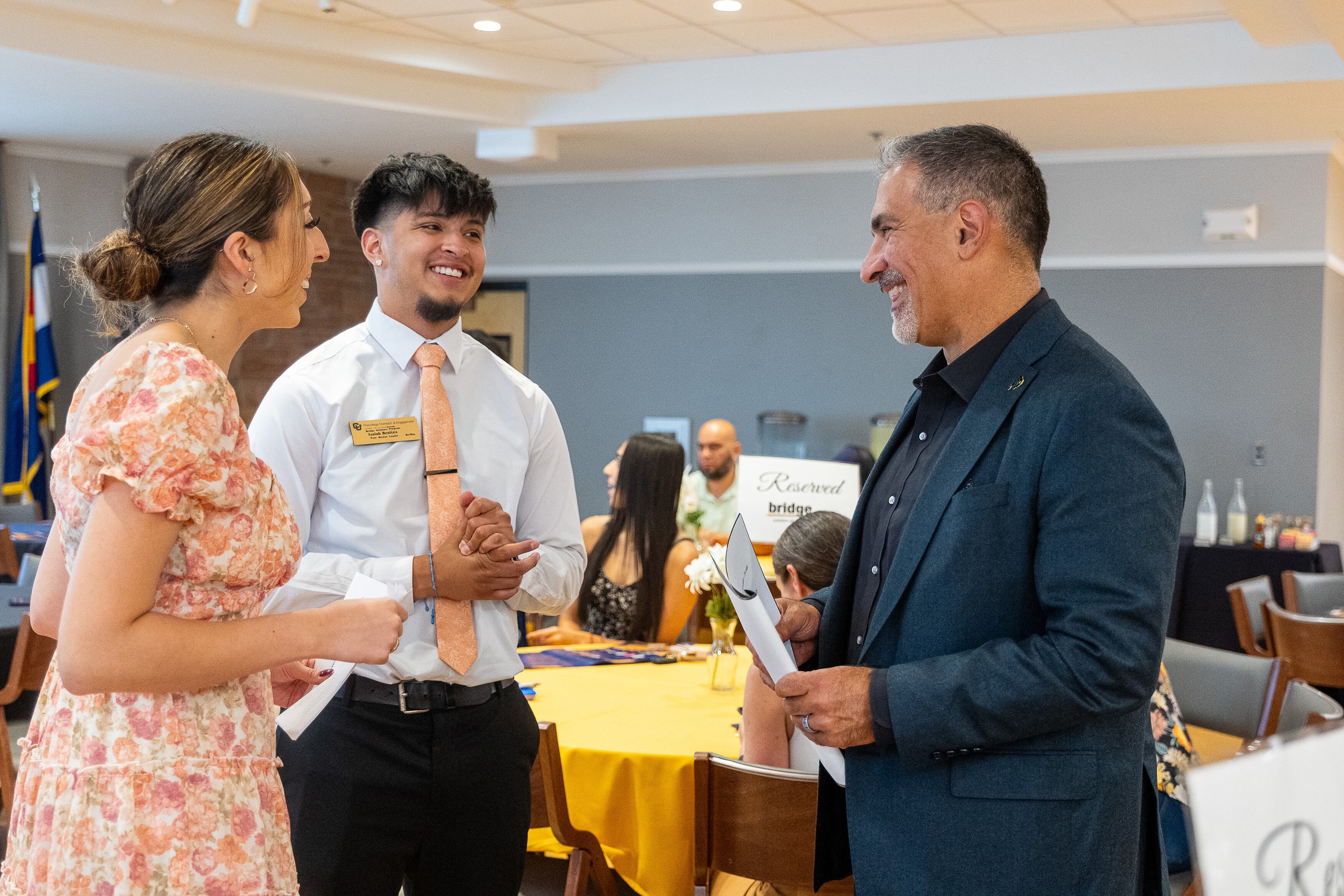 Three people in business clothes stand next to each other talking in a conference room.