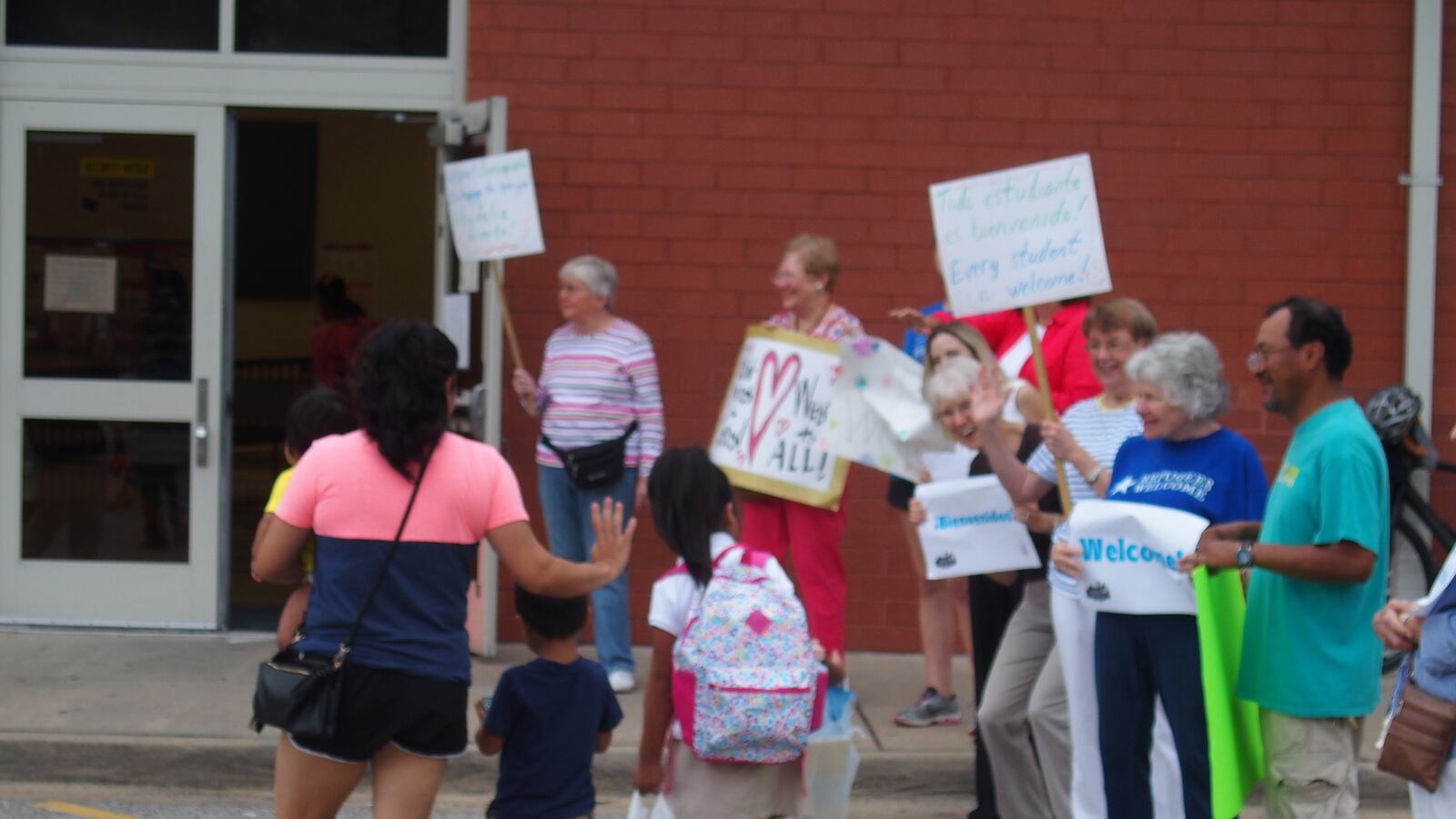 Neighbors, faith leaders and advocacy groups greet immigrant families arriving at Brewster Elementary School on the first day of class in Memphis.