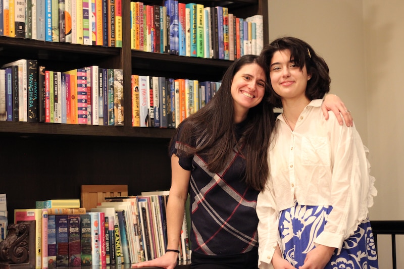An adult woman and a middle school girl stand next to each other in front of a bookshelf.