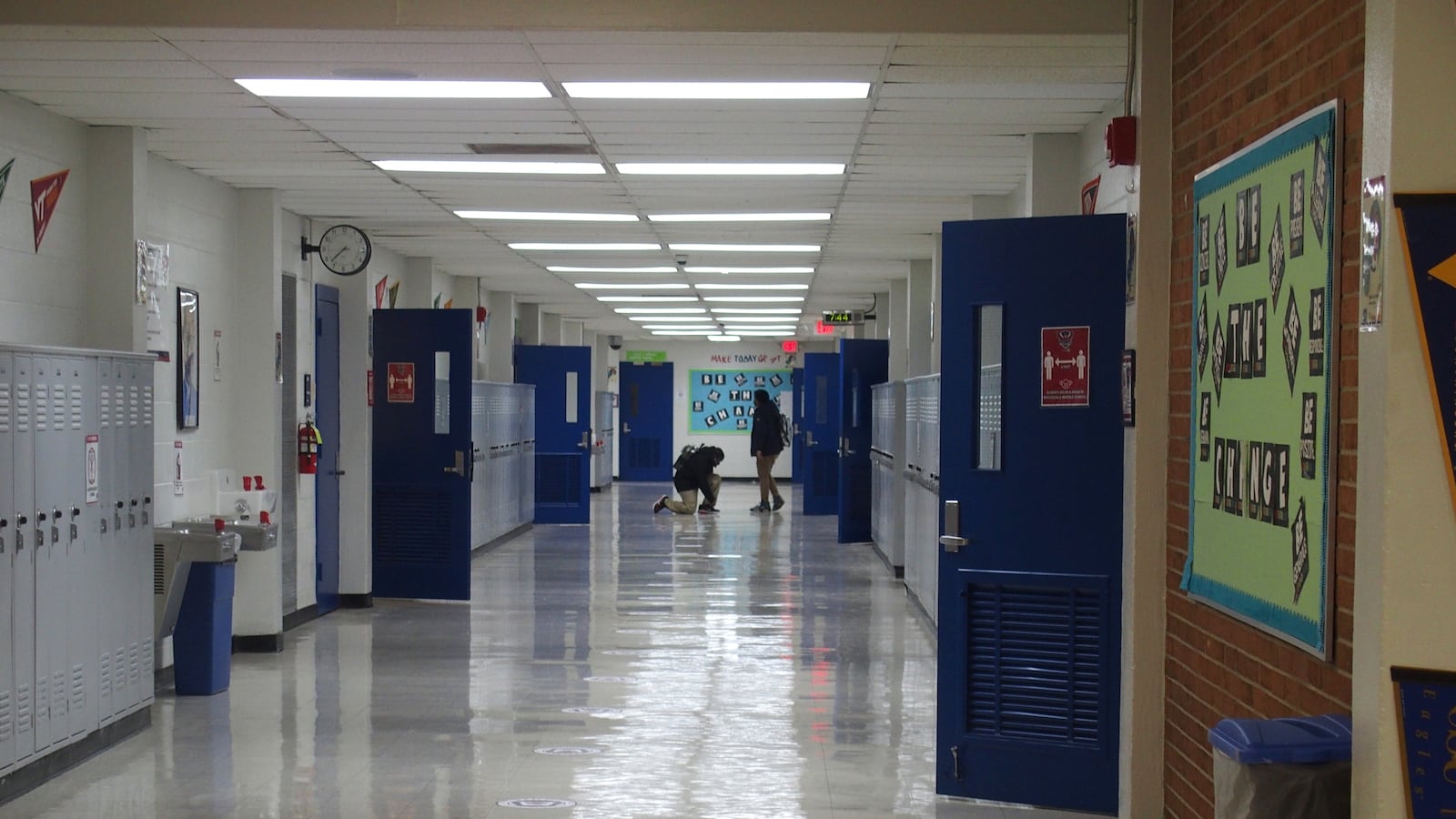 Two students stand at the end of a school hallway.