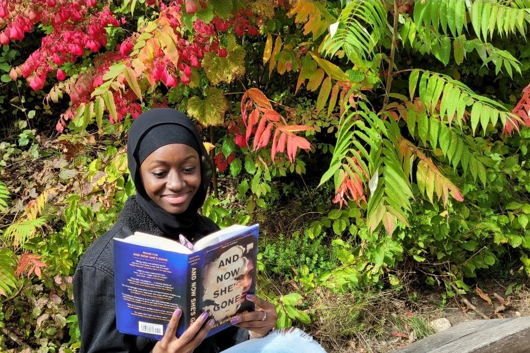 A woman sits on a park bench reading a book.