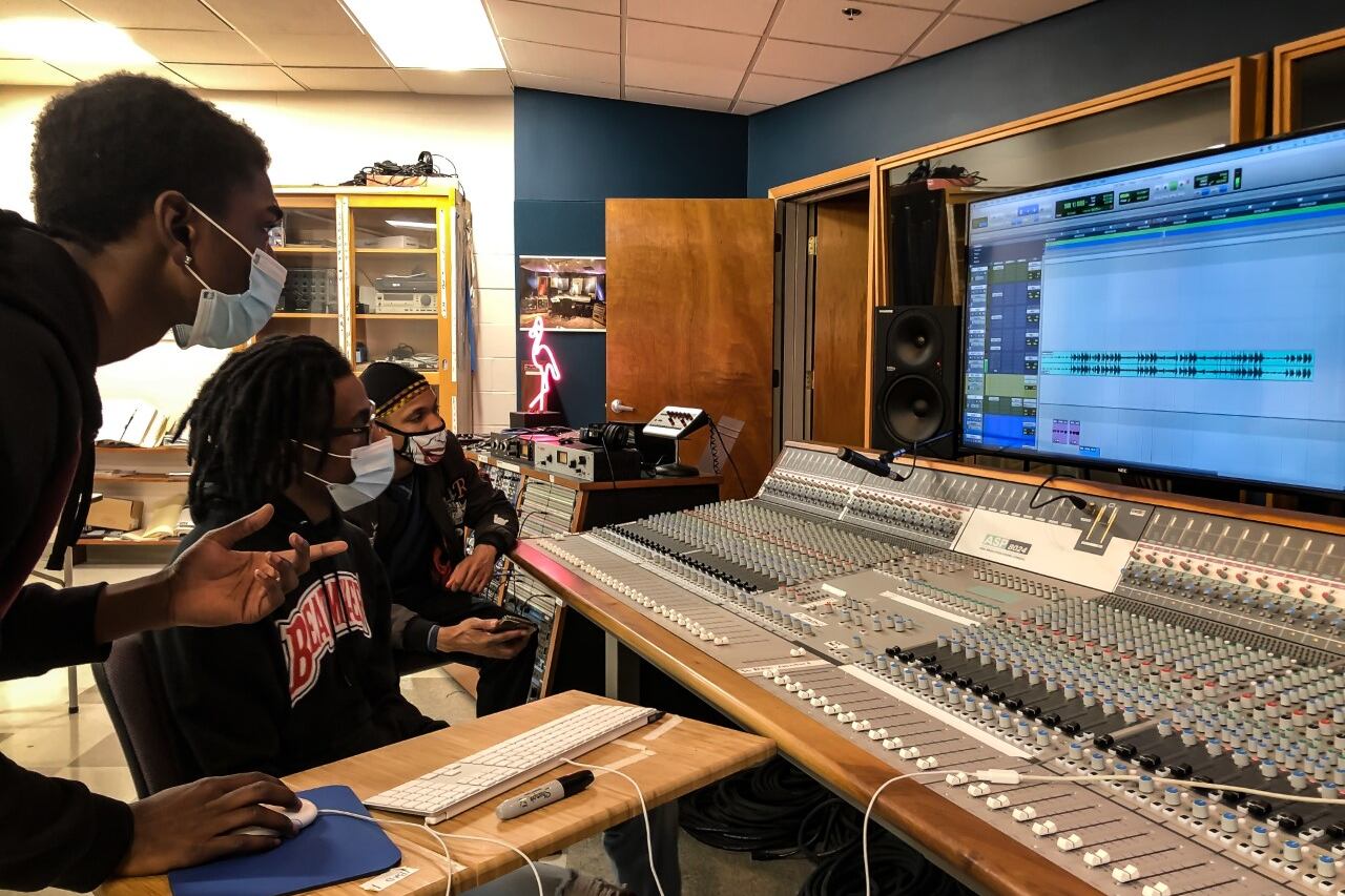 Three Nashville State Community College students, dressed in black sweatshirts and wearing face masks, look at a computer screen while working on a sound board.