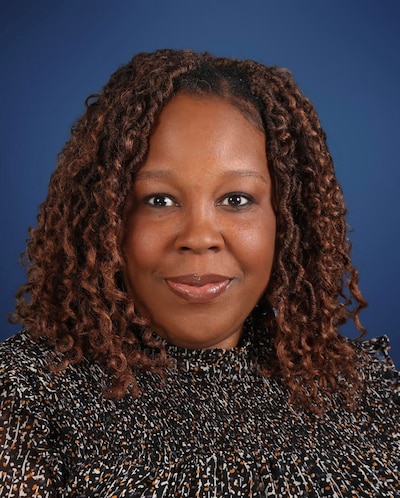 A woman with long dark hair poses for a portrait with a blue background.