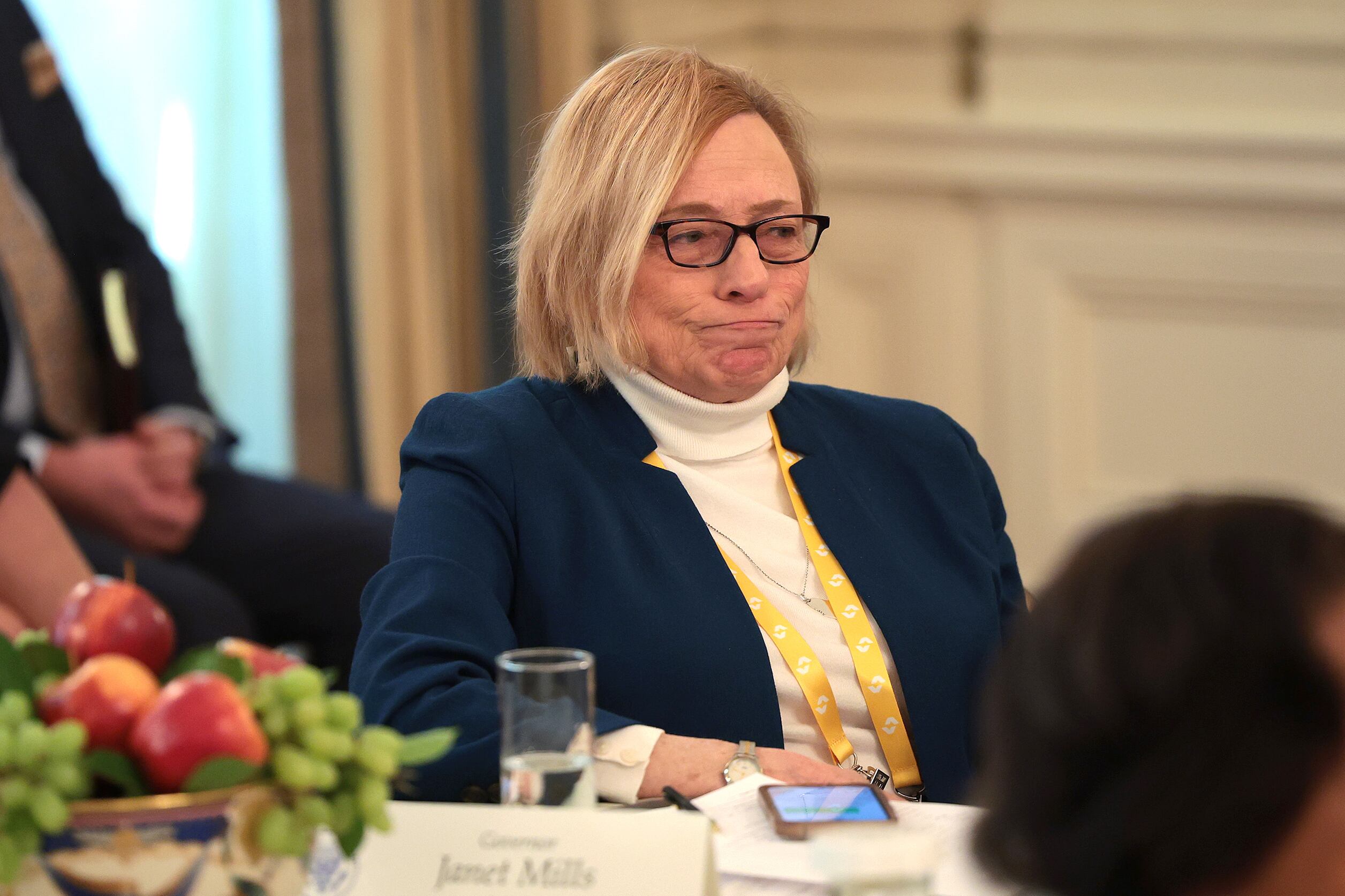 A woman with short blonde hair and wearing glasses sits at a table.