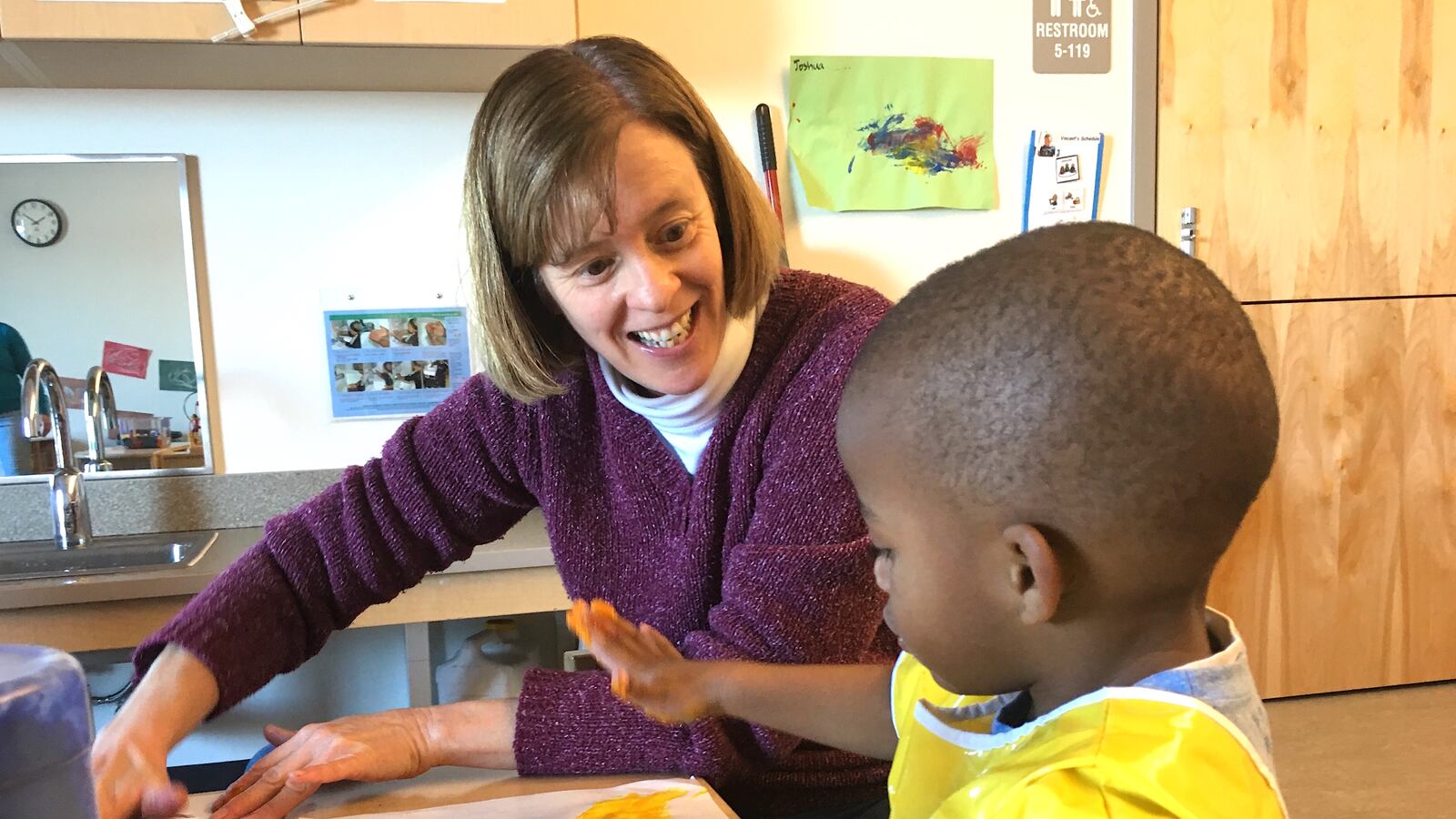 Sandi Polasek, a preschool teacher at a Sewall Child Development Center site in far northeast Denver, finger paints with a student.