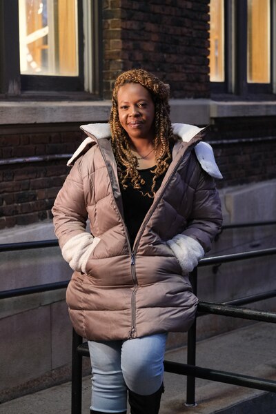 An adult woman wearing a winter jacket stands outside posing for a portrait with a building in the background.
