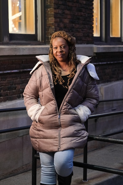An adult woman wearing a winter jacket stands outside posing for a portrait with a building in the background.