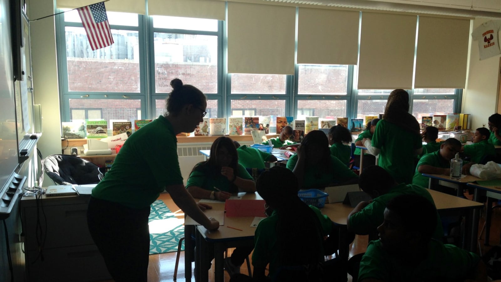 A teacher leans over to help students seated at desks.