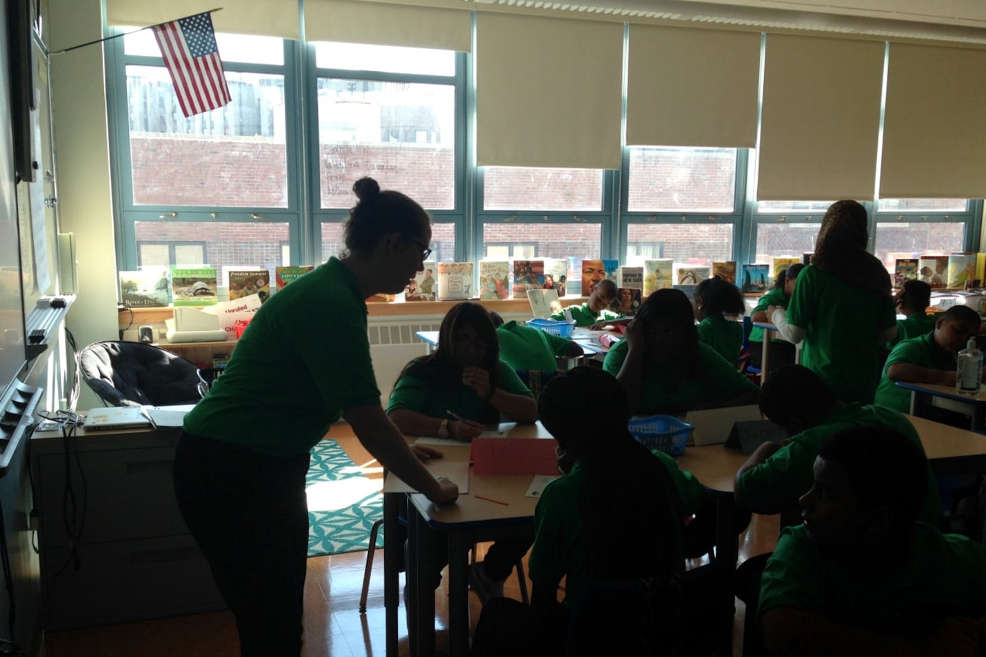 A teacher leans over to help students seated at desks.