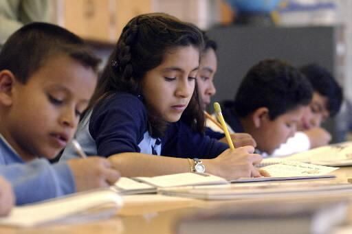 Students sit in line at a table and fill out practice for a standardized test.