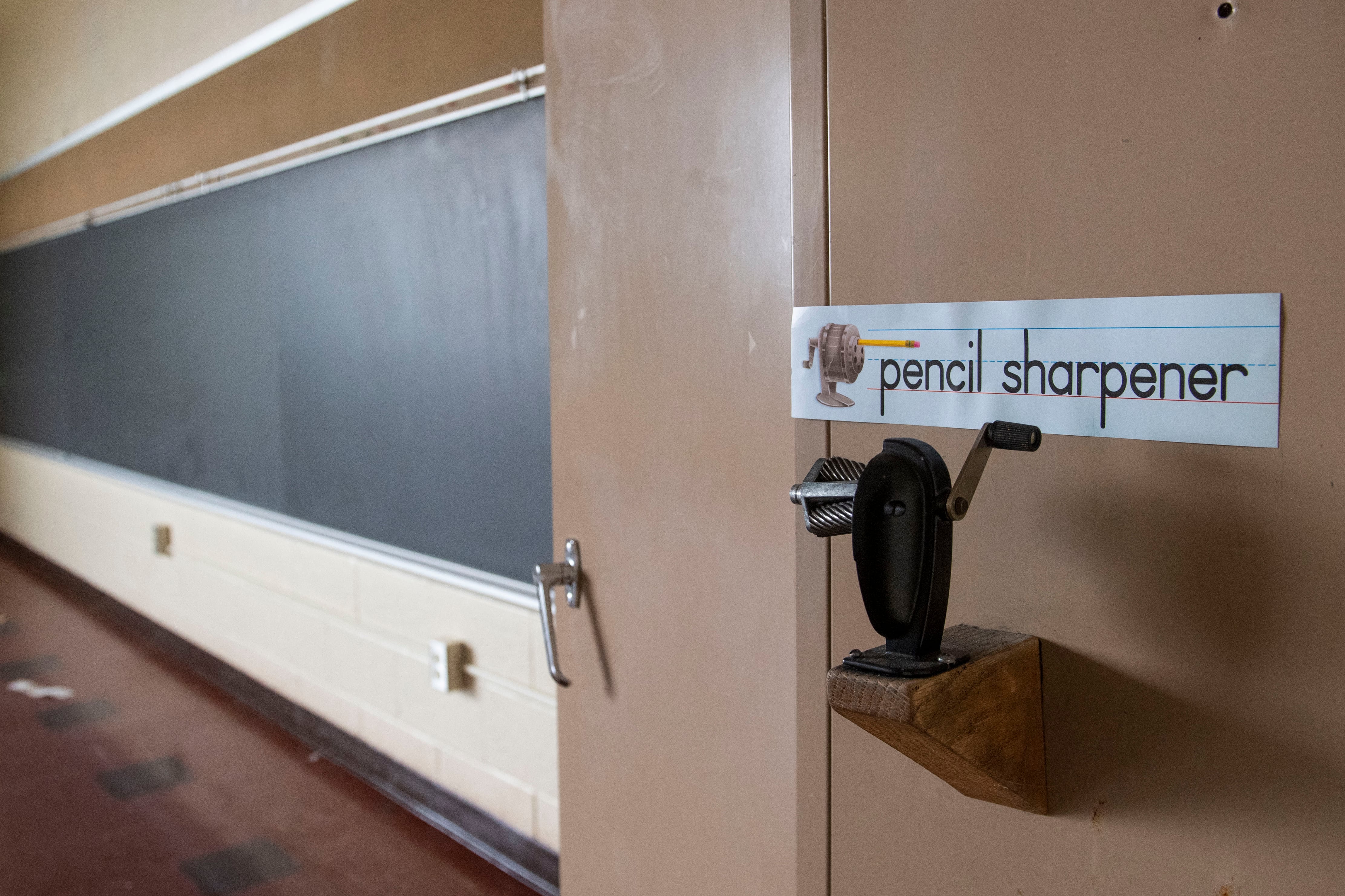 A mechanical pencil sharpener sitting on a wooden block under a sign that reads pencil sharpener