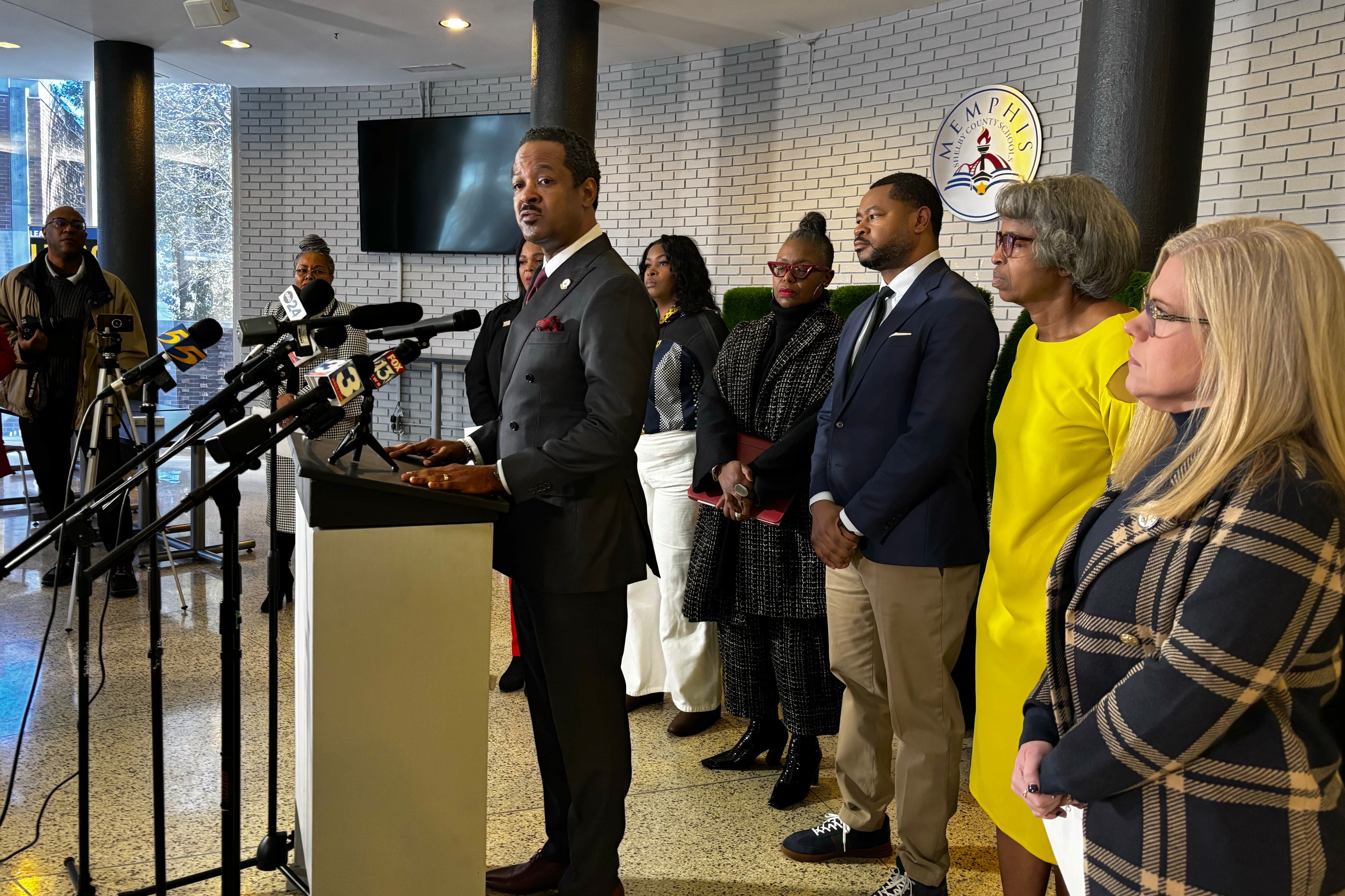 A group of people in business clothes stand behind a speaker at a podium in the lobby of a building.