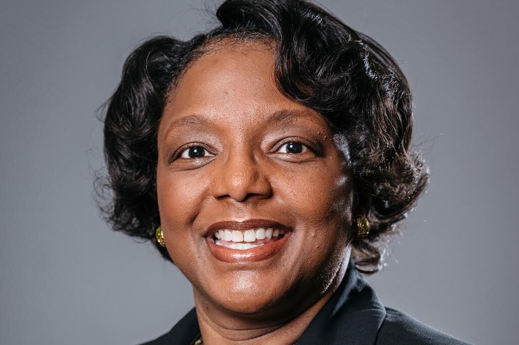 Portrait of a smiling woman wearing a dark jacket and jewelry.