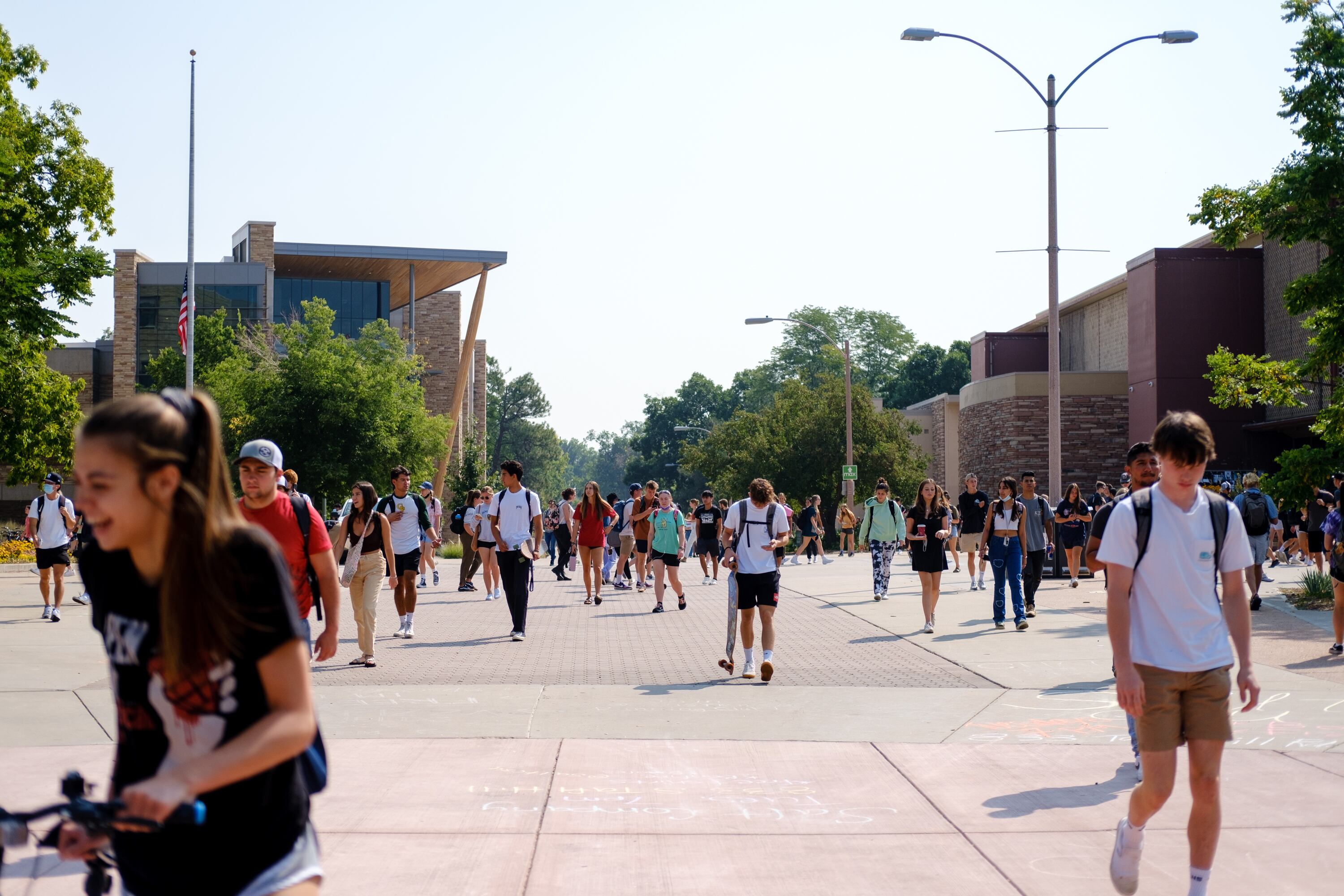 Students walk down a large brick pathway on Colorado State University’s campus. The sun shines on the students in the late summer.