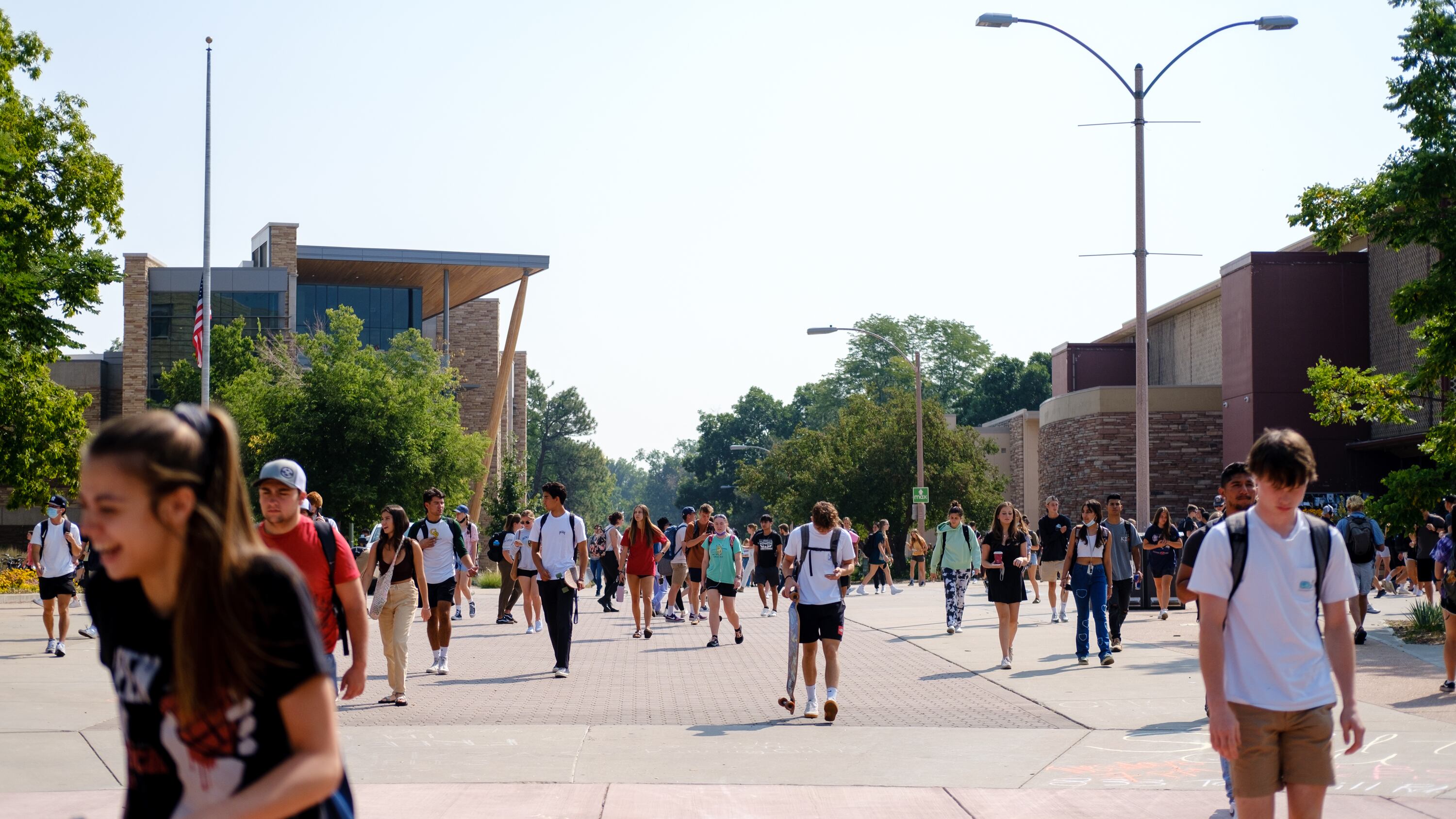 Students walk down a large brick pathway on Colorado State University’s campus. The sun shines on the students in the late summer.