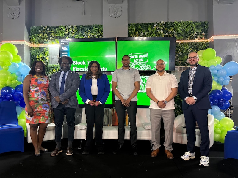 A photograph of a group of people in business clothes standing in a row for a portrait in front of four tv screens.