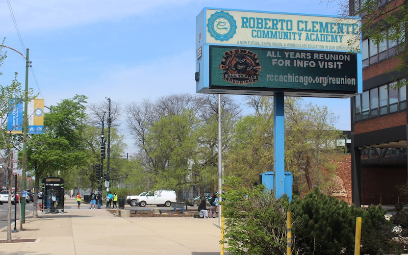 A large white and green sign outside with trees in the background.