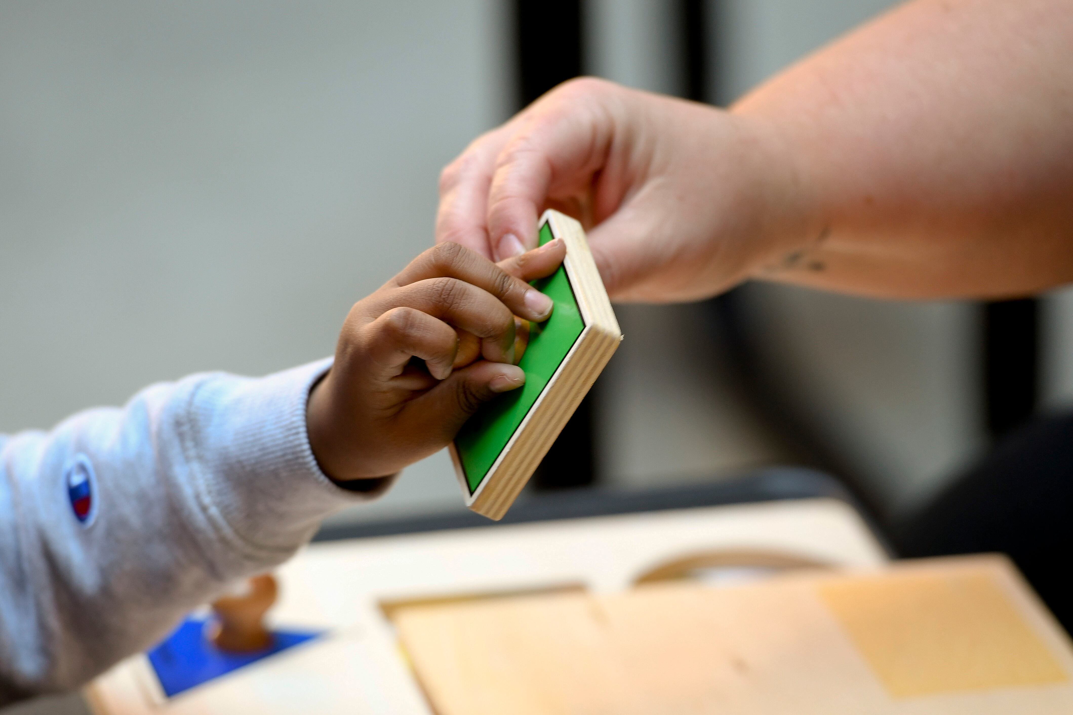 A special education student reaches a hand out for a block, held by his teacher.