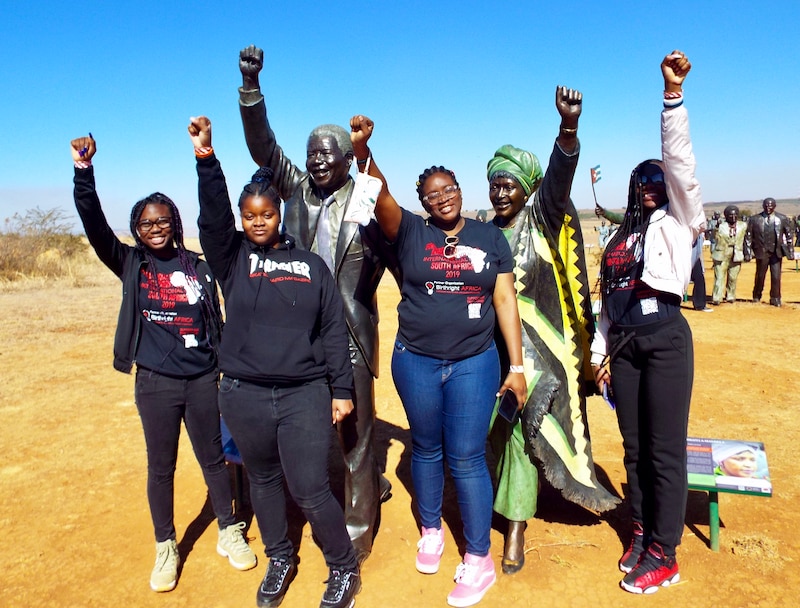 A group of high school students pose with their fists proudly in the sky outside and in front of a memorial in Cape Town.