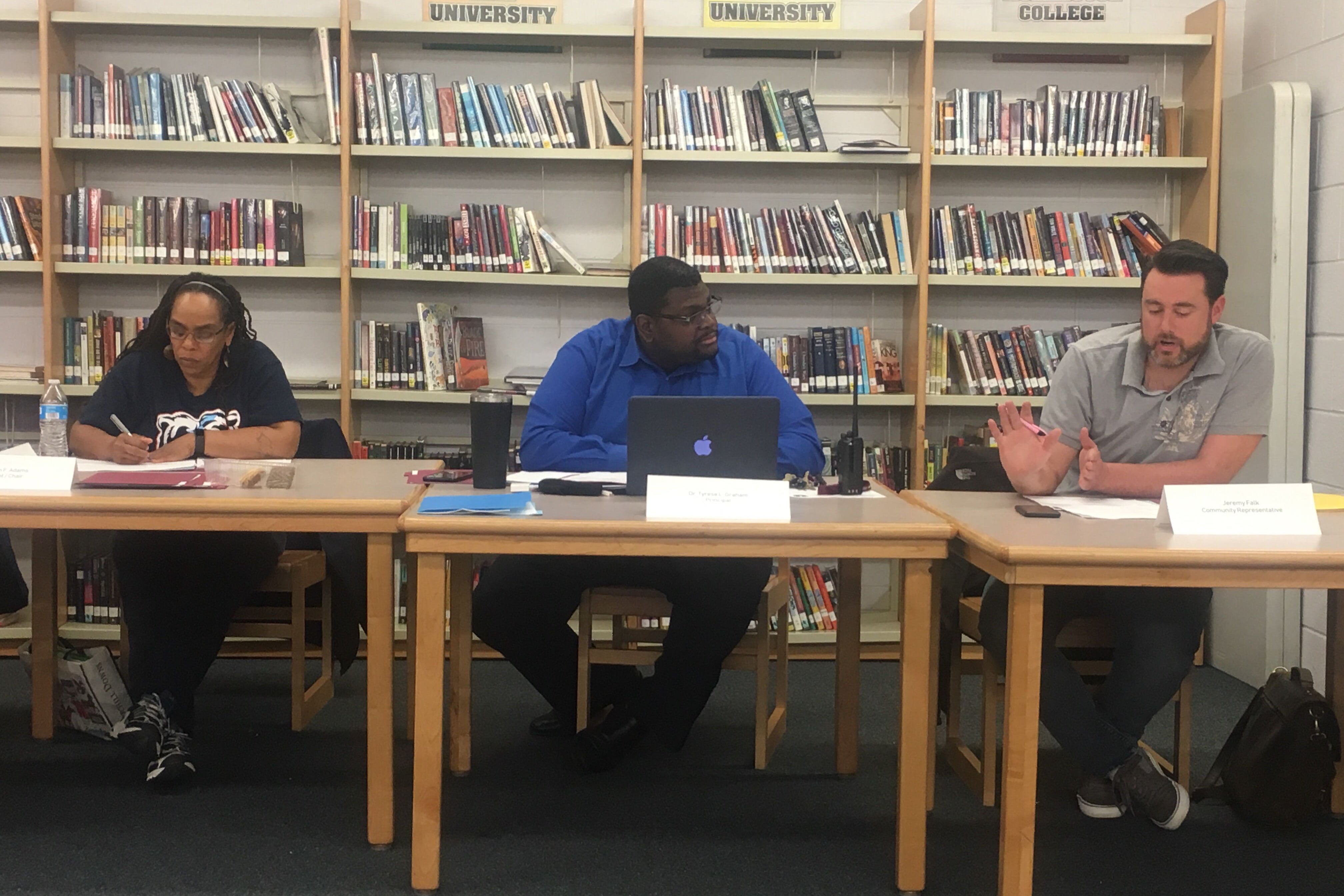 Three people sit at tables in a school library during a meeting in Chicago.