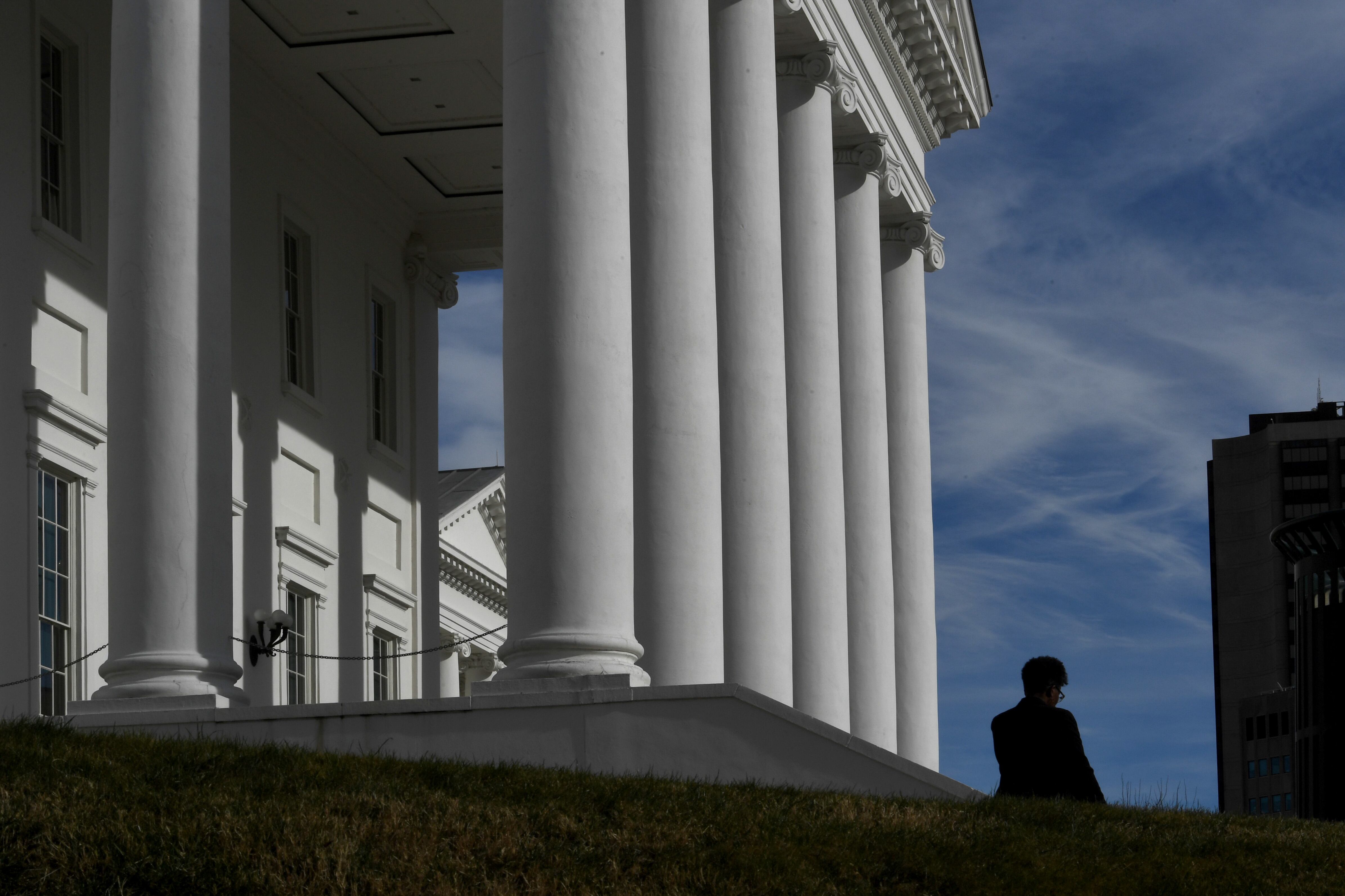 An ornate white building with columns shown against a blue sky with clouds and a single person shown in shadow.
