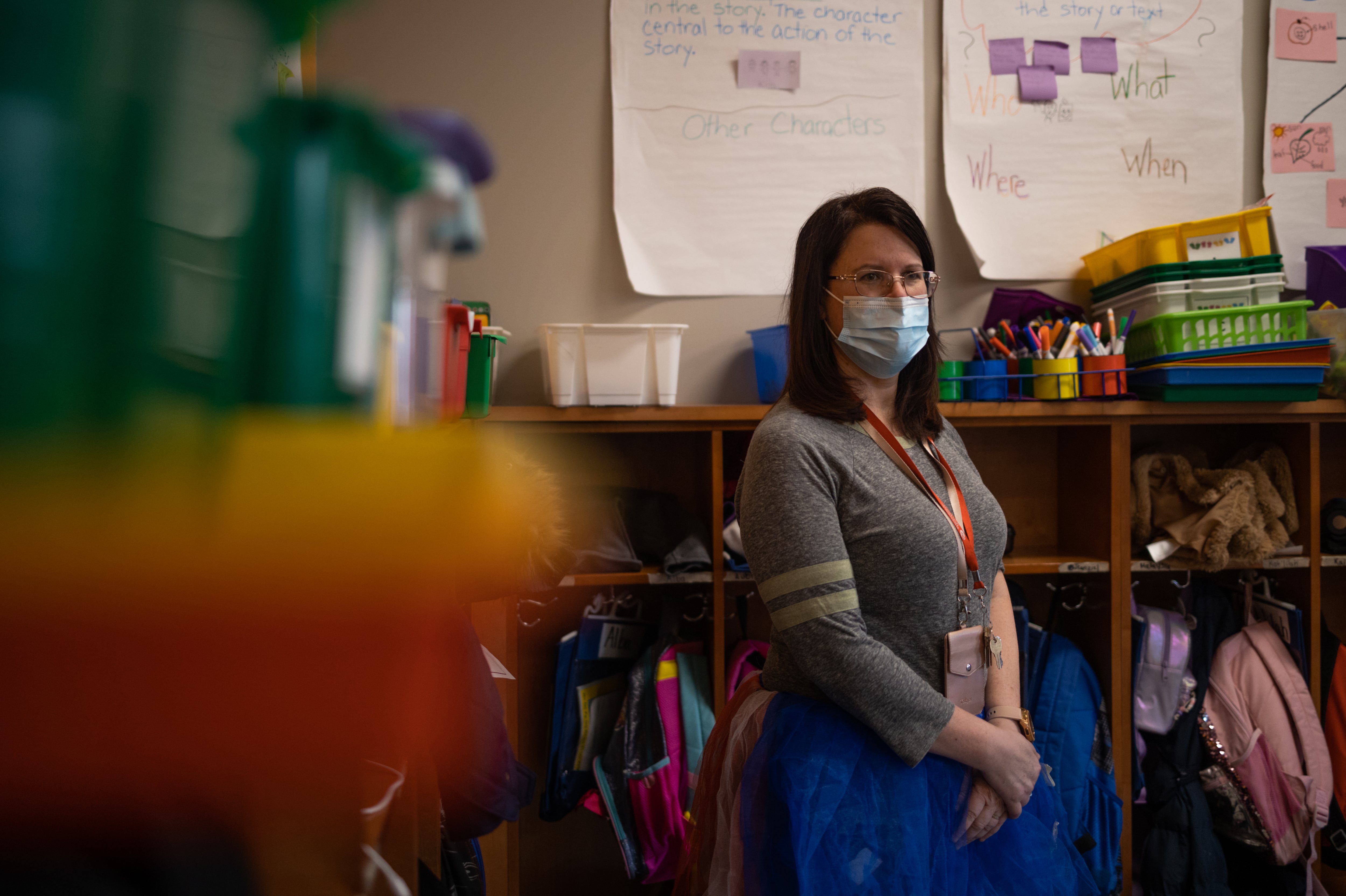 Teacher Ruth Llorens stands in front of book cases and wears face mask inside her classroom at Cayuga Elementary School.