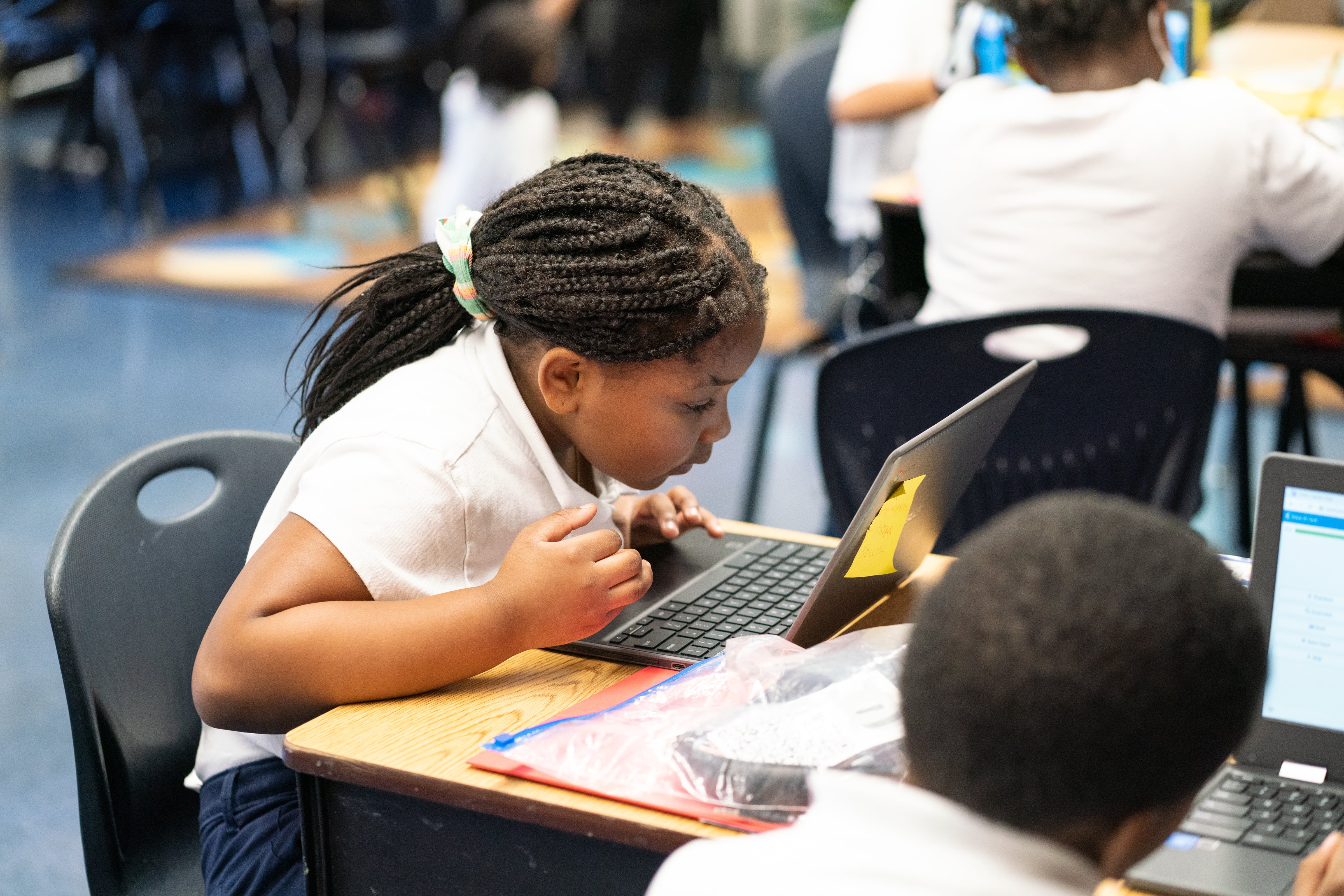 A girl works on her laptop amongst other students in the classroom.