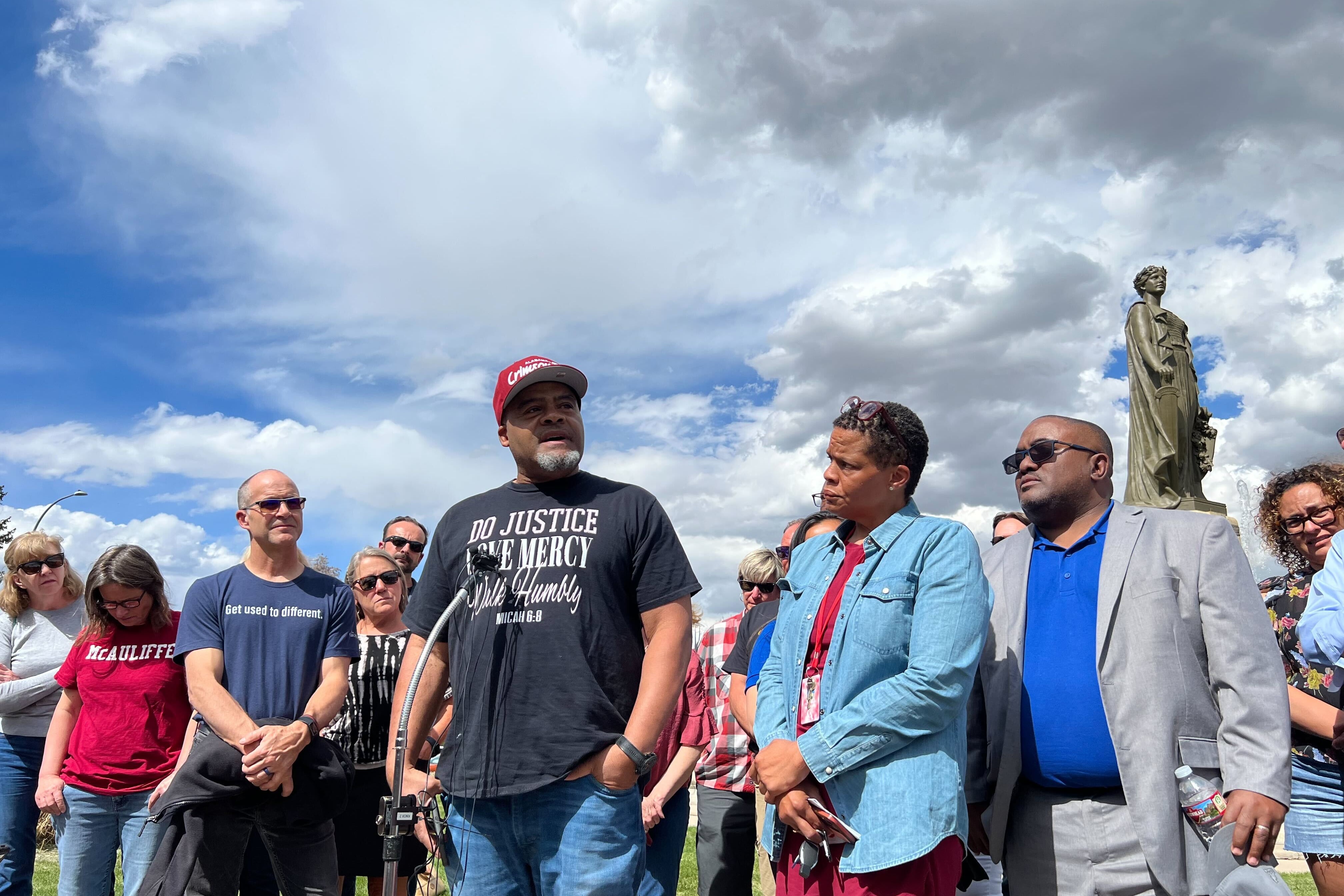 A man with a red cap stands in the middle of a group of people under sky with heavy clouds.