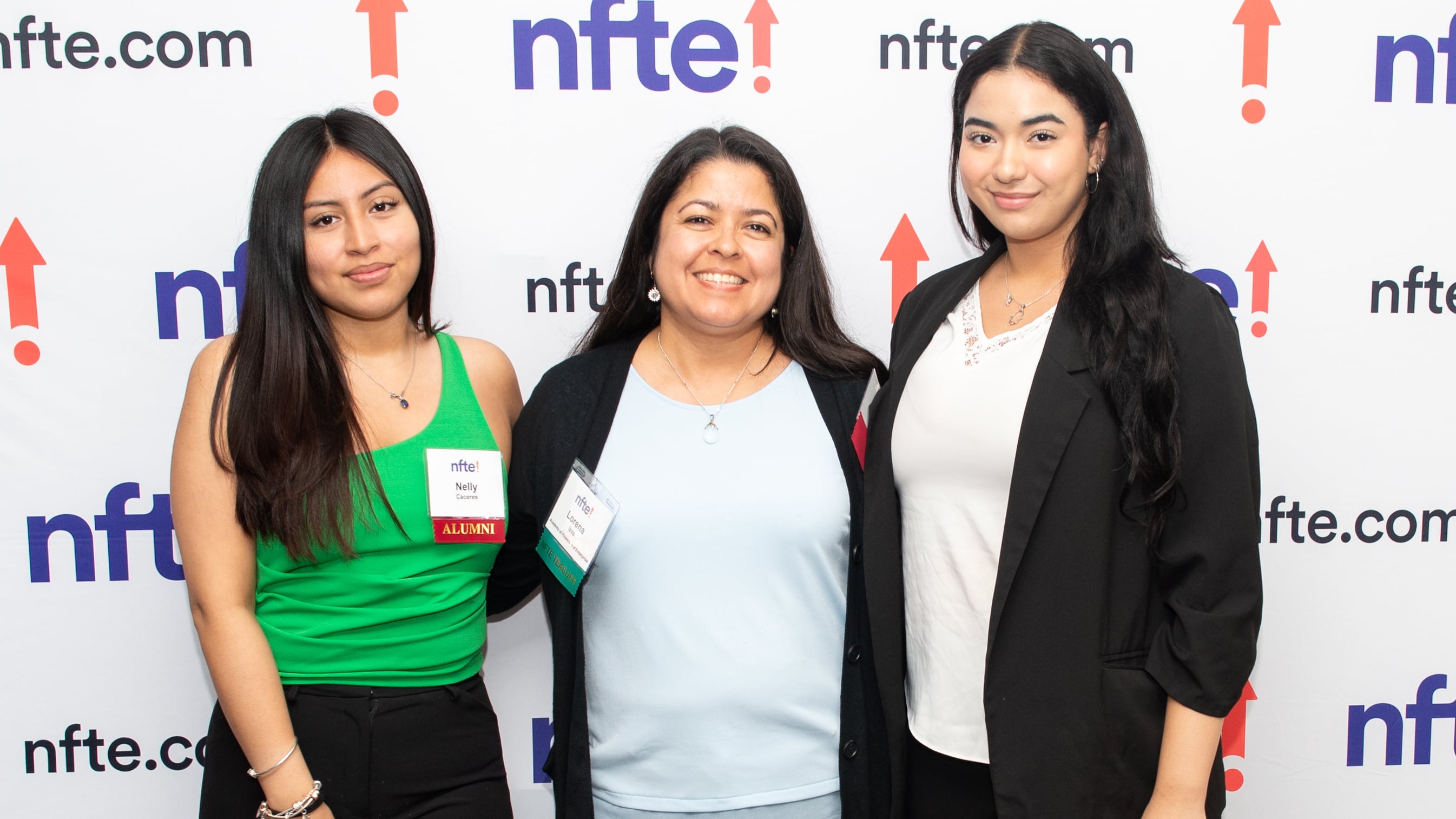 Three women with long black hair pose for picture in front of a wall that says "NFTE."