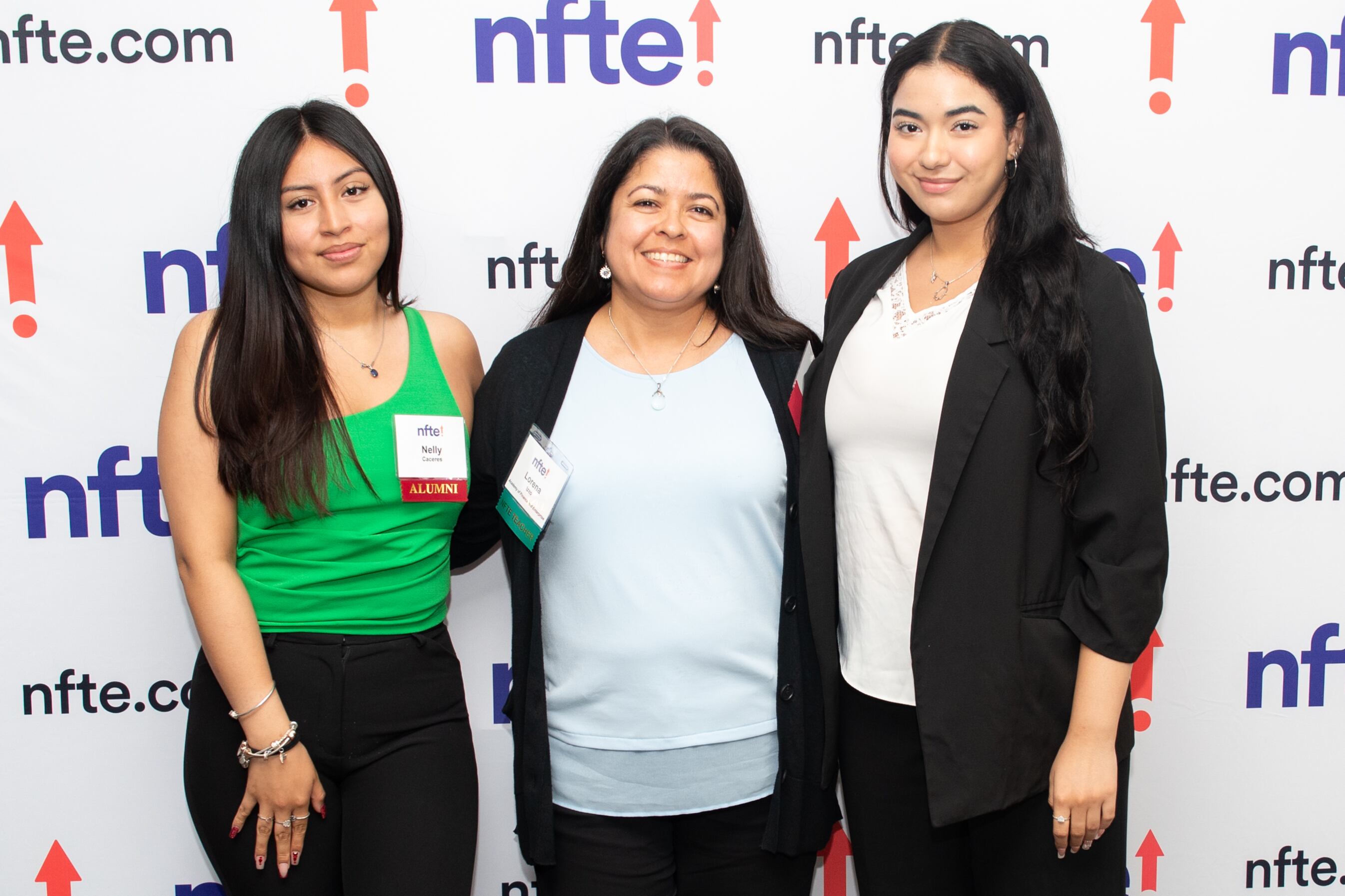 Three women with long black hair pose for picture in front of a wall that says "NFTE."