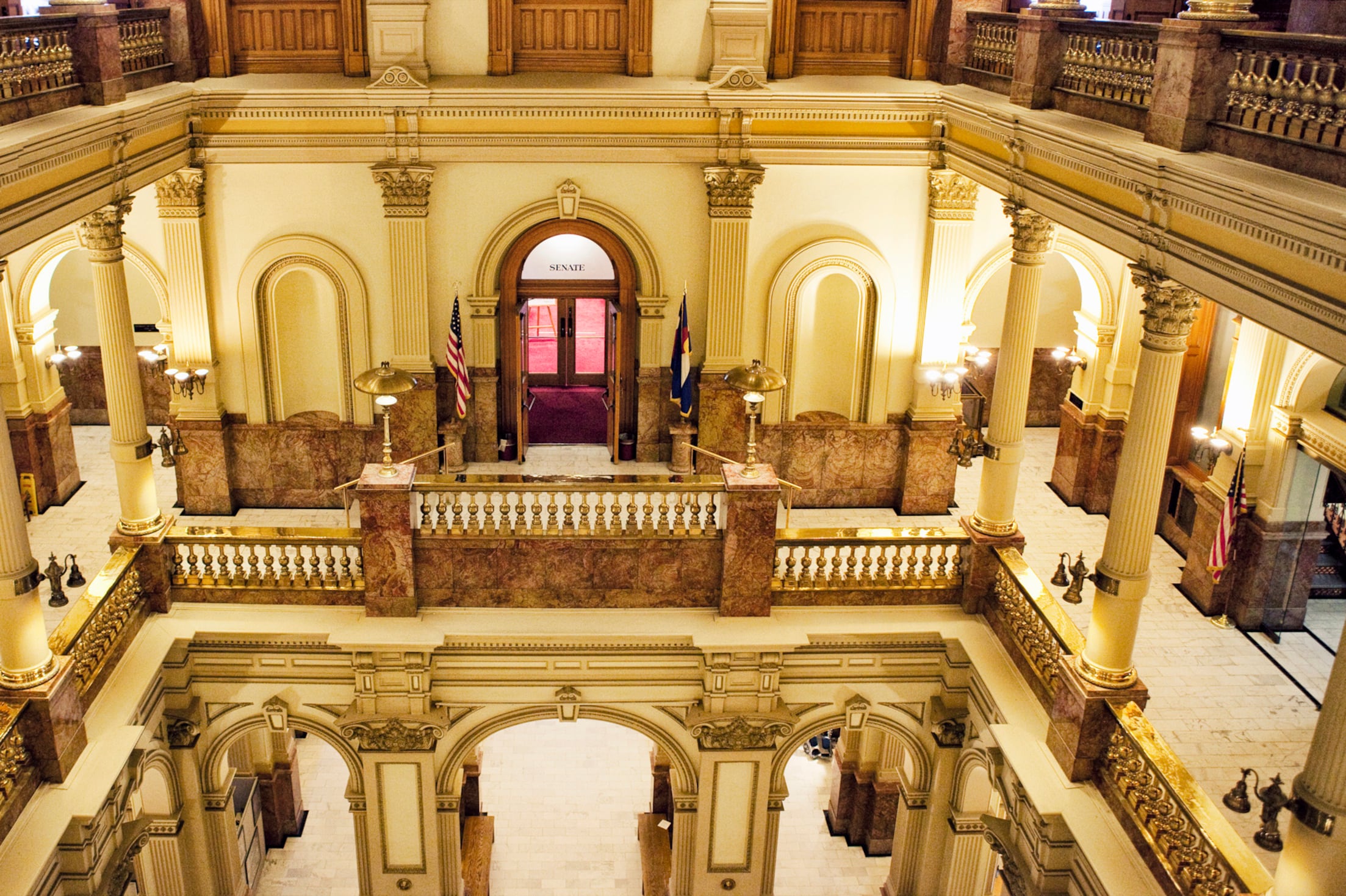 An inside view of the Colorado Capitol building with light stone walls and pillars and wooden doors and features.