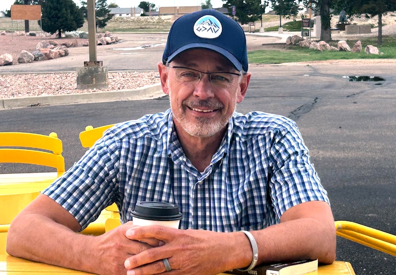 A man in a blue cap and a blue checked shirt sits at a yellow table.